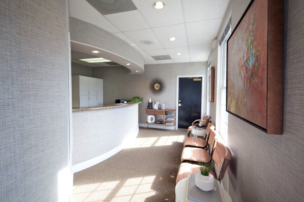 Bright modern office waiting room with curved reception desk, chairs, and wall art.