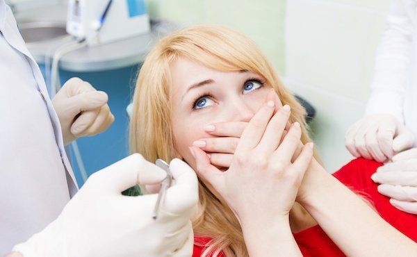 Angstpatientin beim Zahnarzt: Eine ängstliche Frau hält sich die Hände vor den Mund