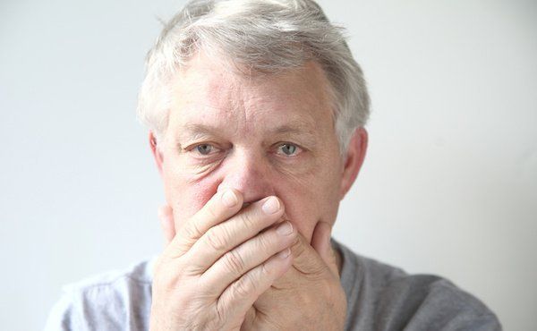Mann mit Mundgeruch hält sich die Hand vor den Mund