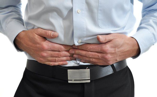 Mann hält sich die Hände vor den Bauch, weil er Magenbeschwerden und Bauchschmerzen hat.