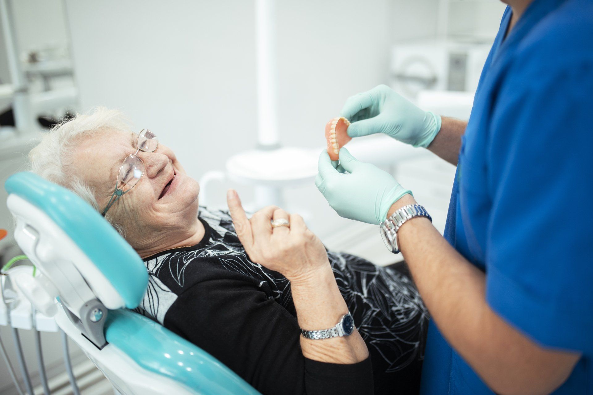 Dentist showing dentures to a smiling patient in a dental chair.