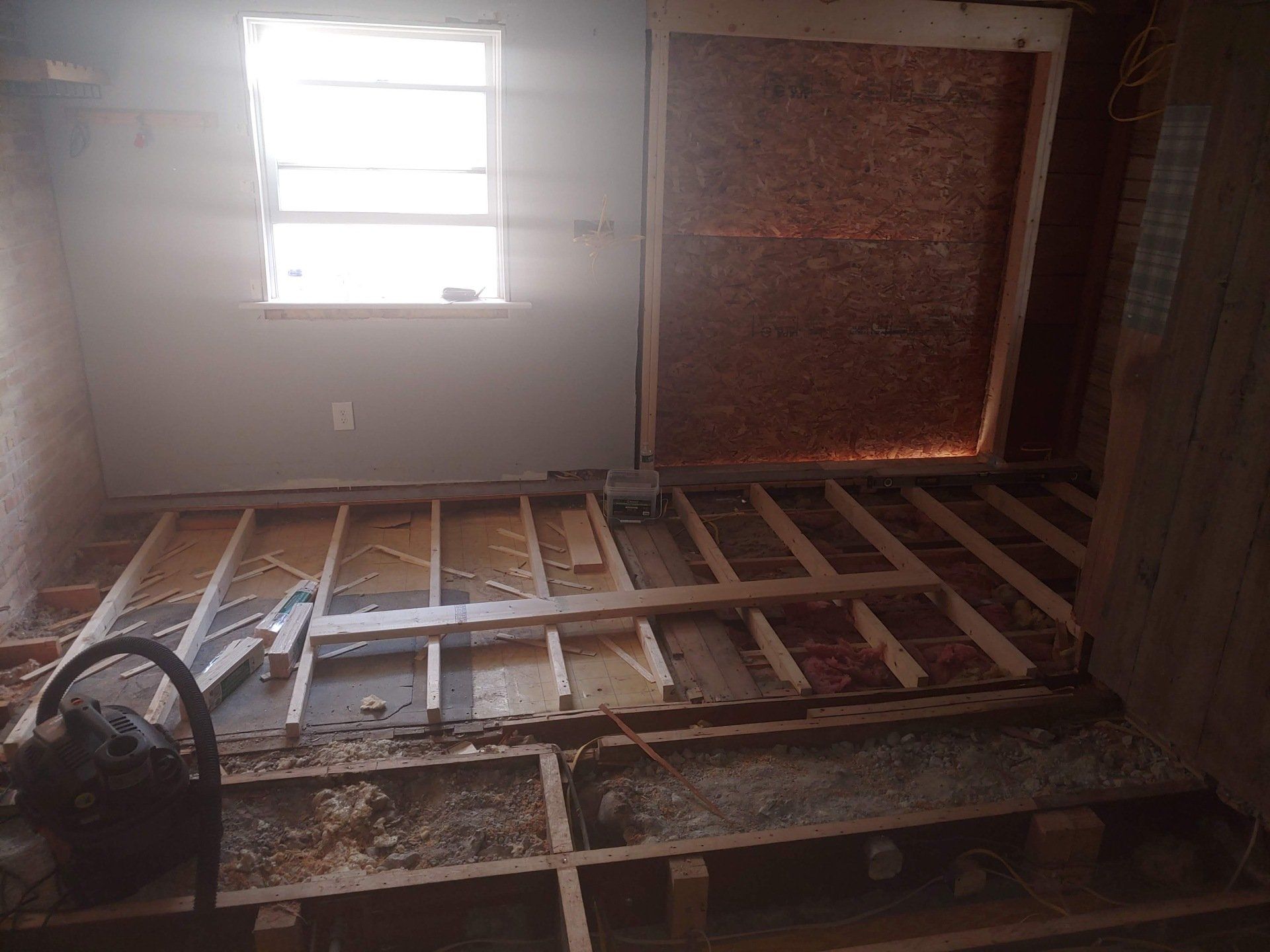 Partially demolished room with exposed floor joists, debris, a window, and a covered opening.