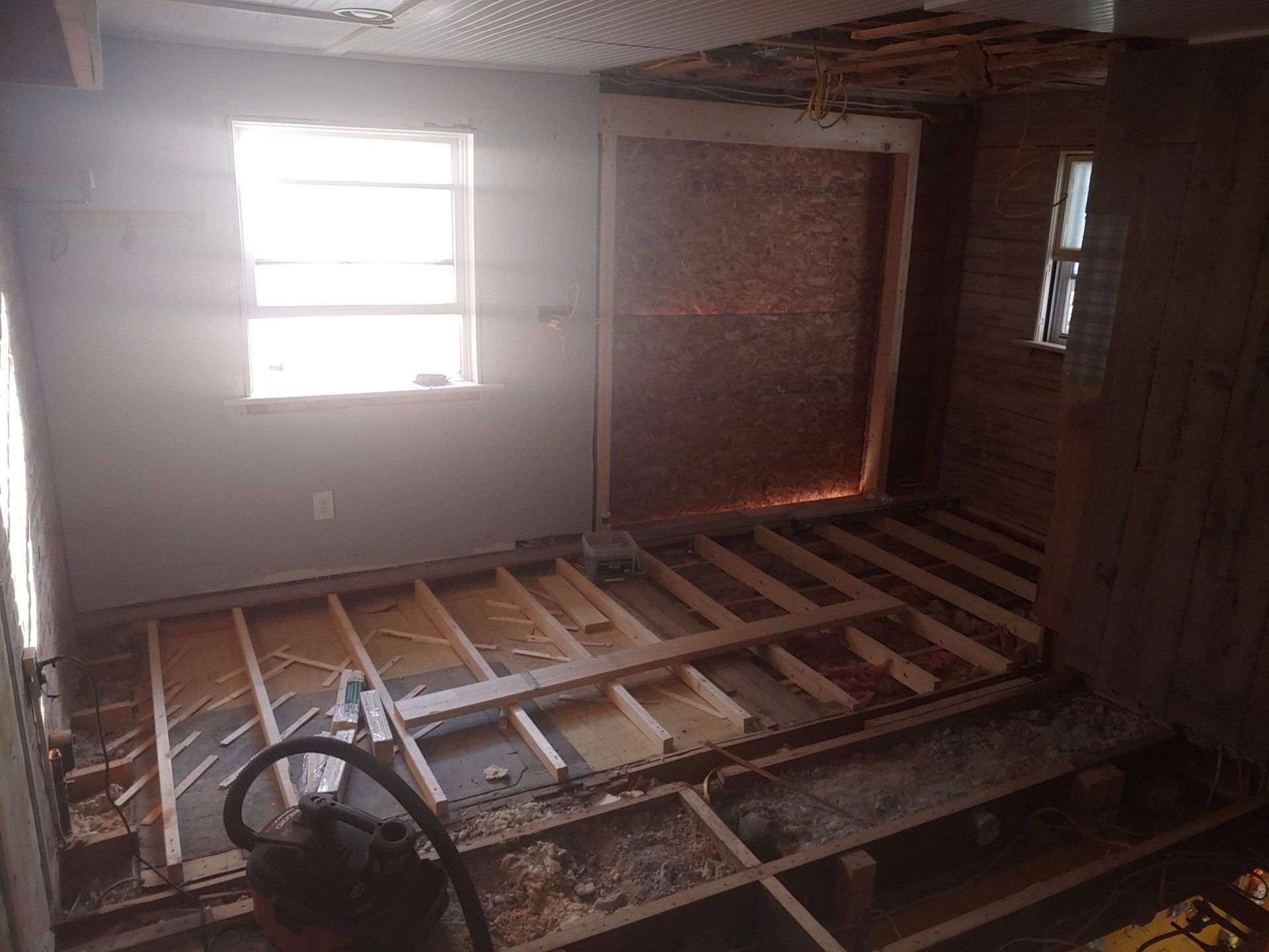 Partially demolished room with exposed floor joists, a window, and construction debris.
