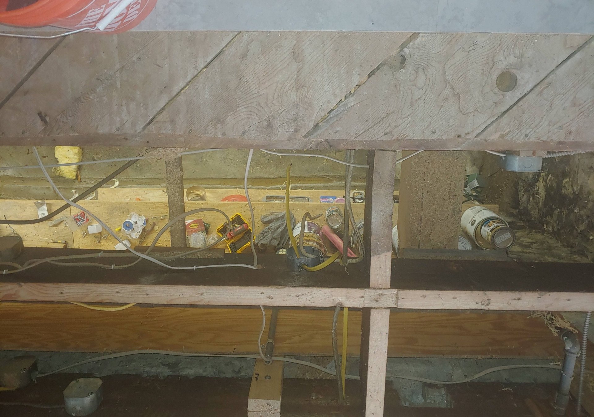 Exposed wiring and electrical components inside an unfinished wall cavity beneath a wooden beam.