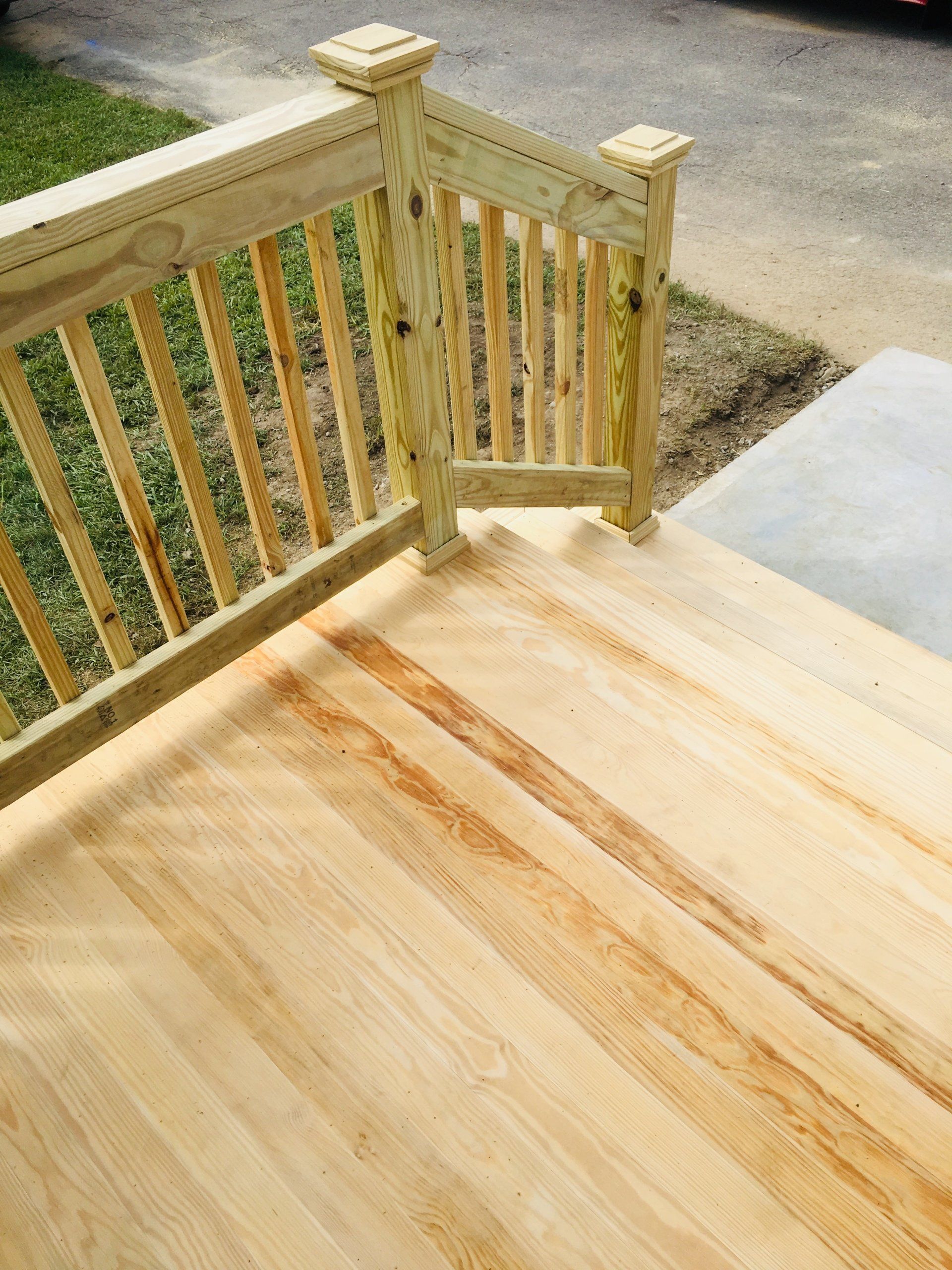 Wooden porch deck with freshly stained floor and railing beside a concrete walkway
