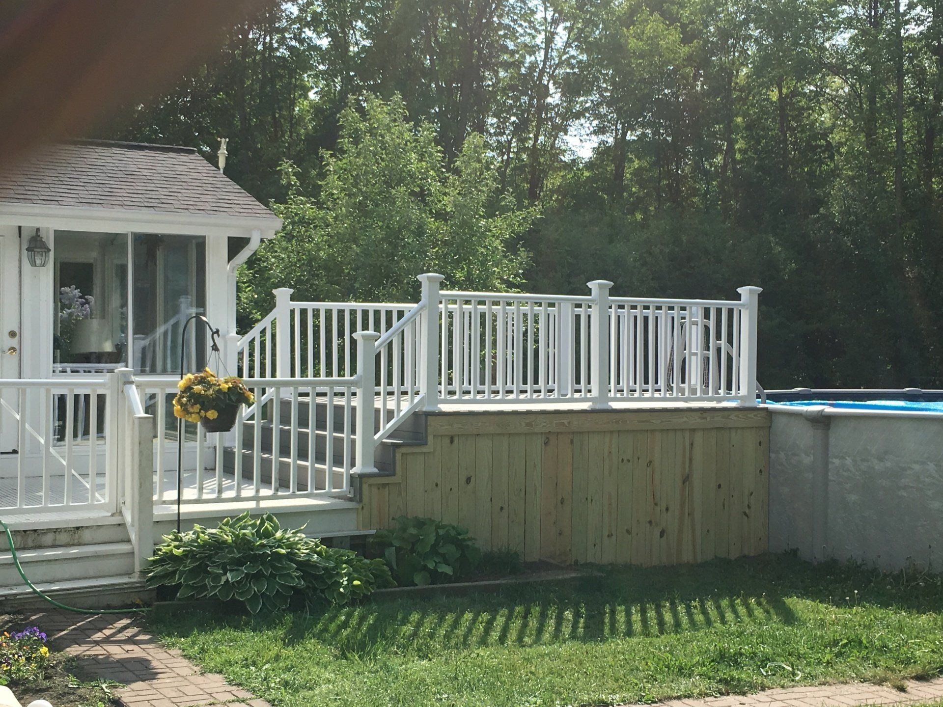 Backyard deck with white railings, steps, and a small above-ground pool beside a house.