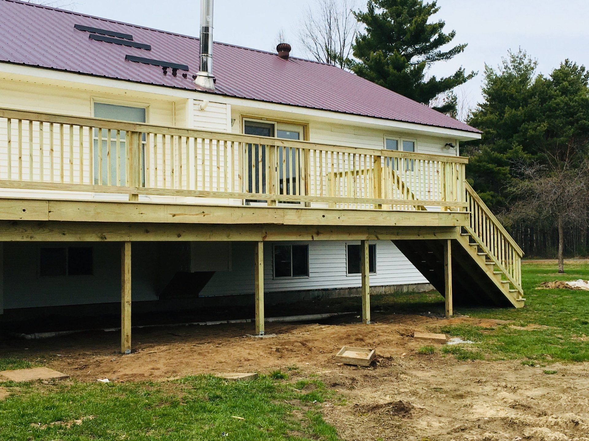 Raised wooden deck on a white house with stairs and railing, set on a grassy yard.