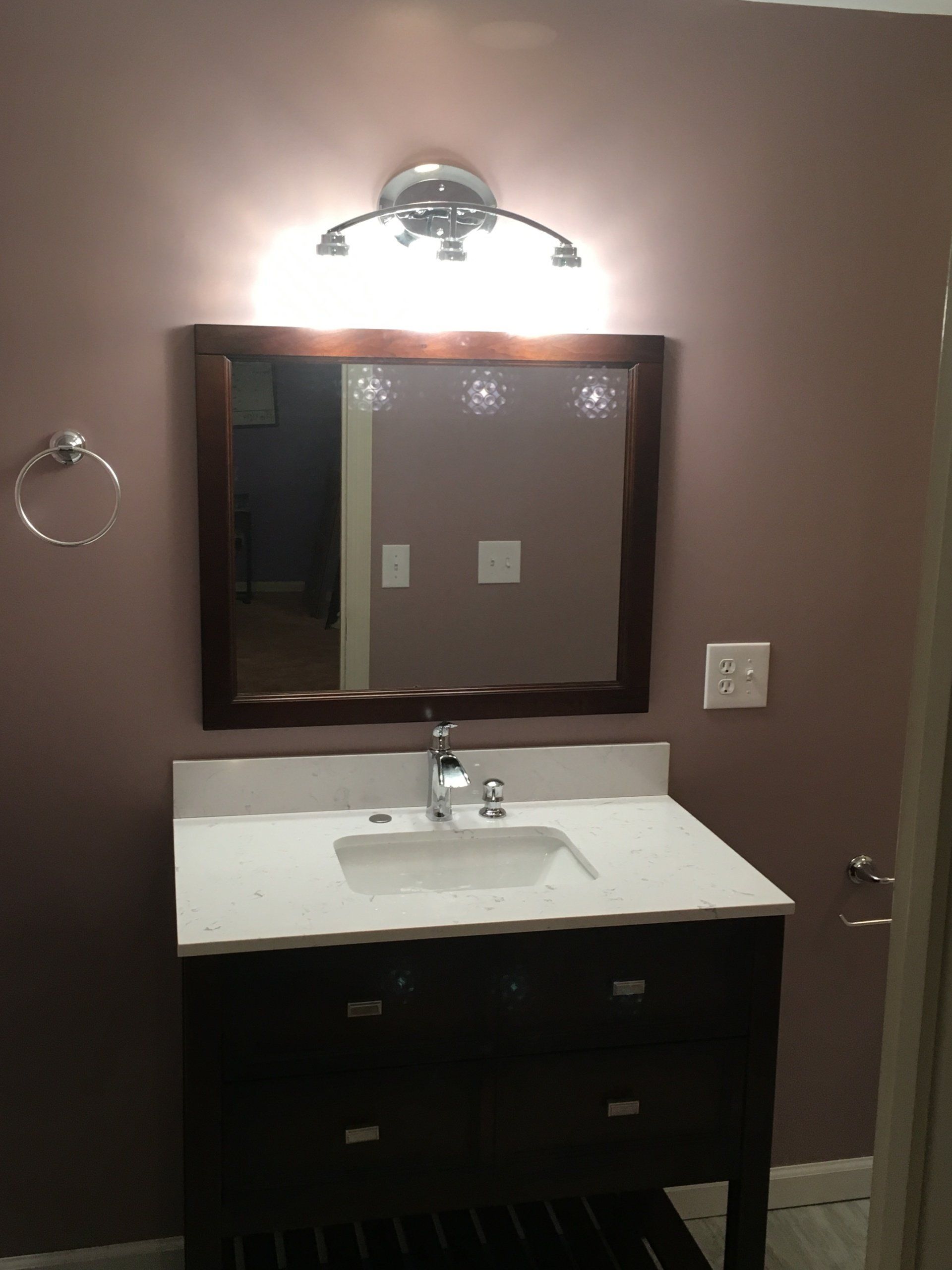 Bathroom vanity with mirror, wall light, sink, and dark cabinets against brown walls.
