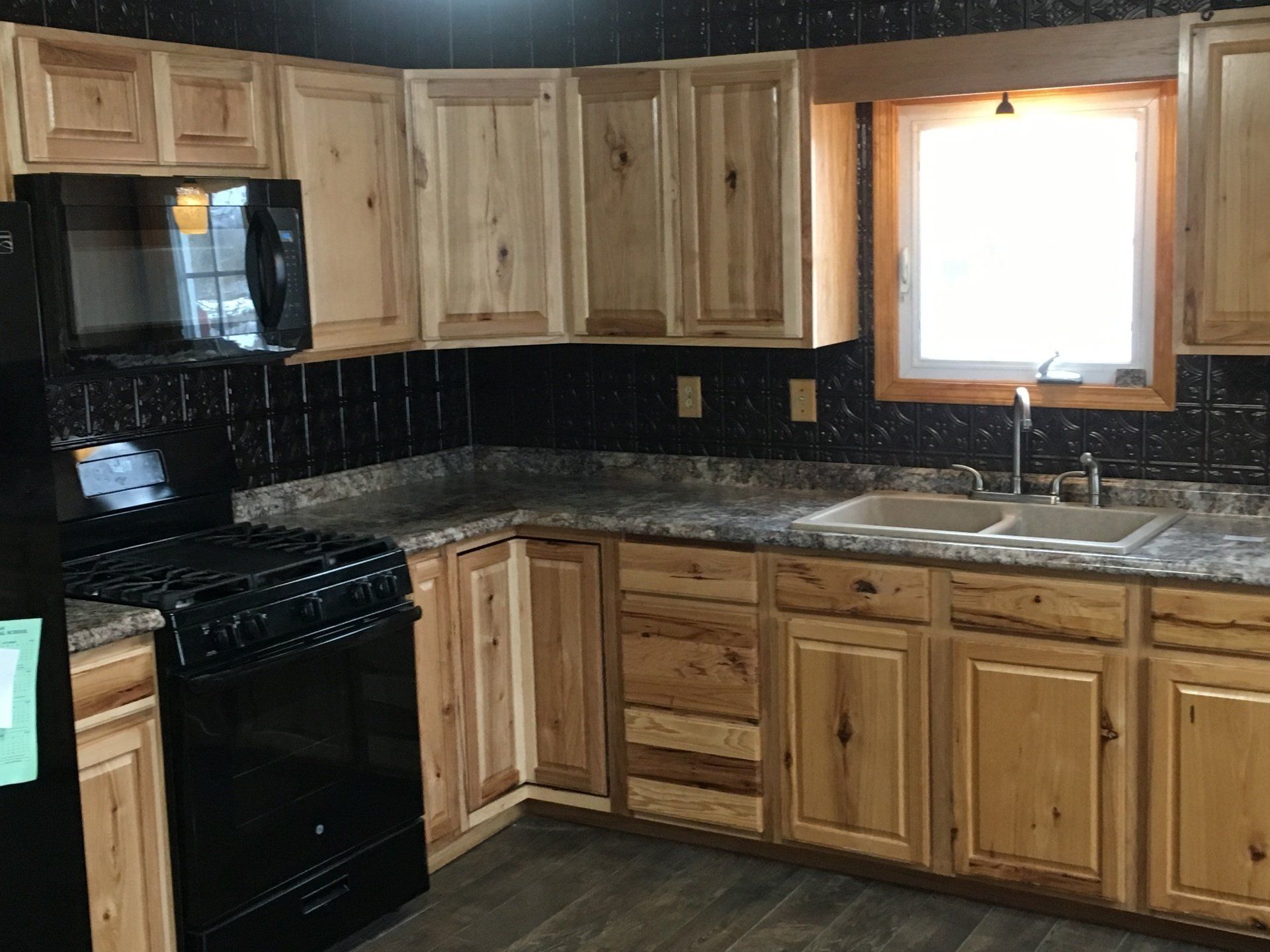 Rustic kitchen with black appliances, wood cabinets, granite counters, and a bright window over the sink