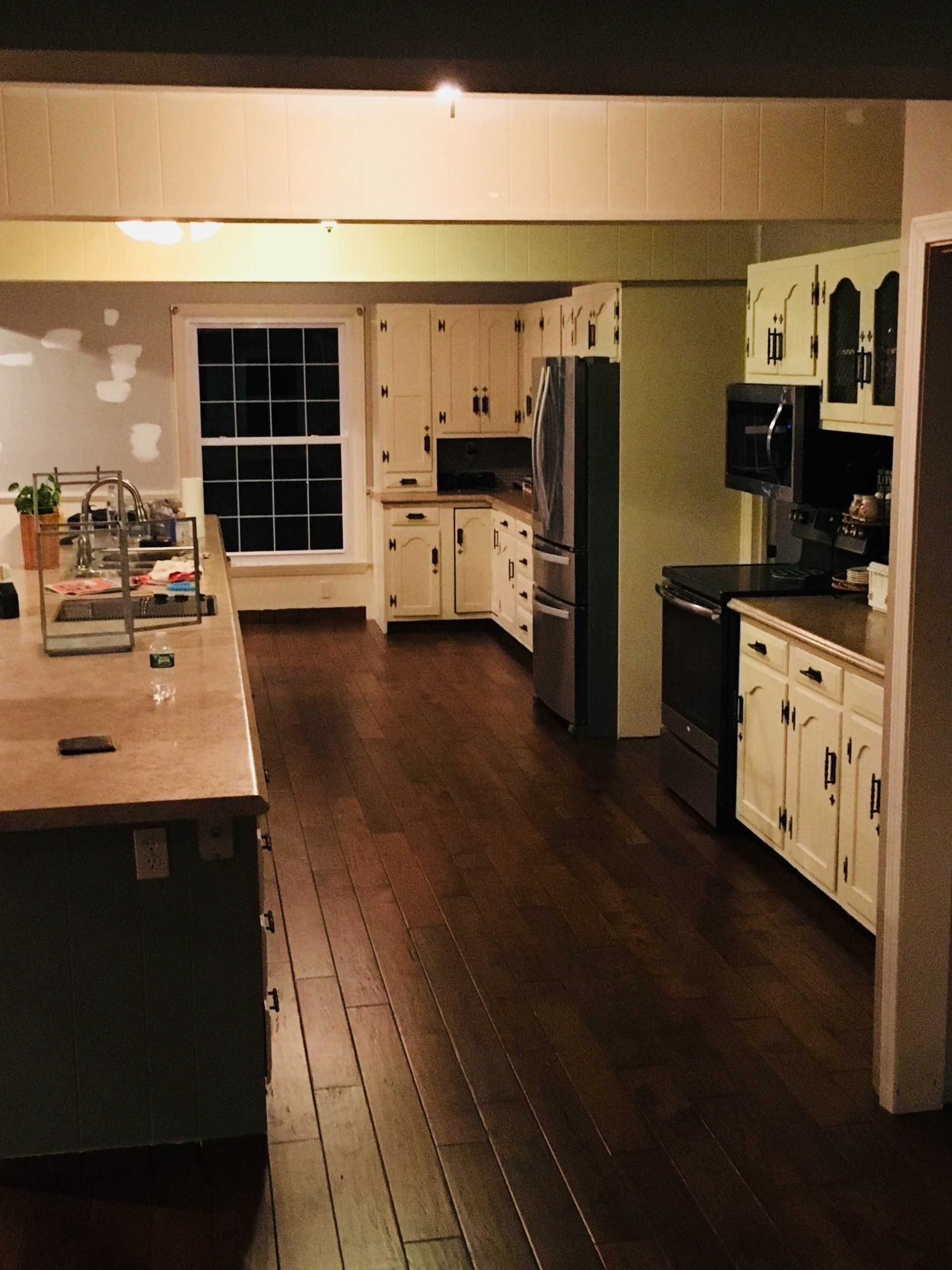 Empty kitchen with dark wood floor, cream cabinets, and a large island under warm lighting.
