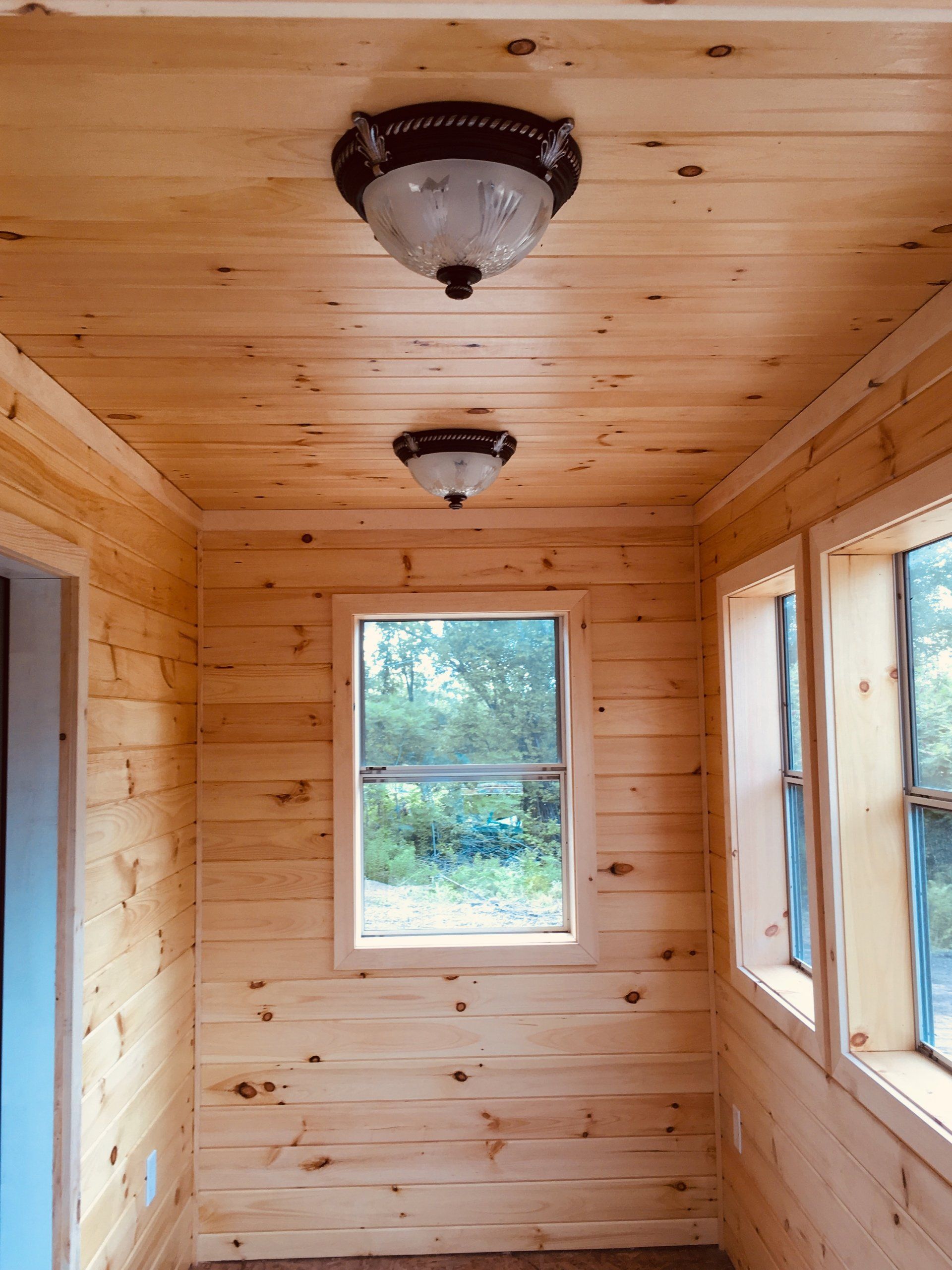 Wood-paneled small room with two ceiling lights and windows showing trees outside