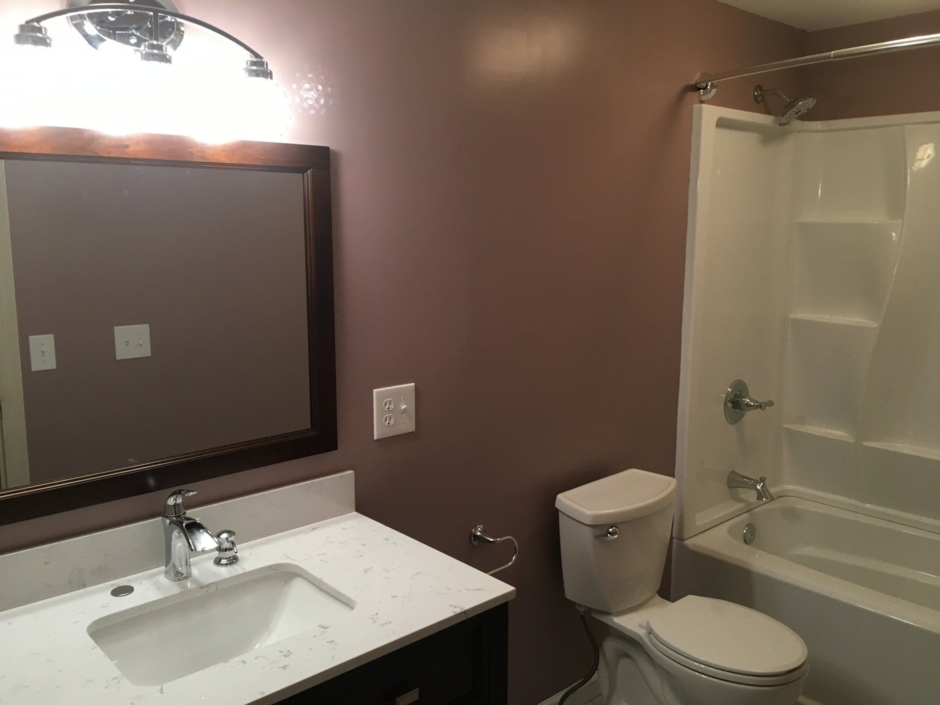 Bathroom with vanity sink, large mirror, toilet, and shower-tub combo in brown and white finishes