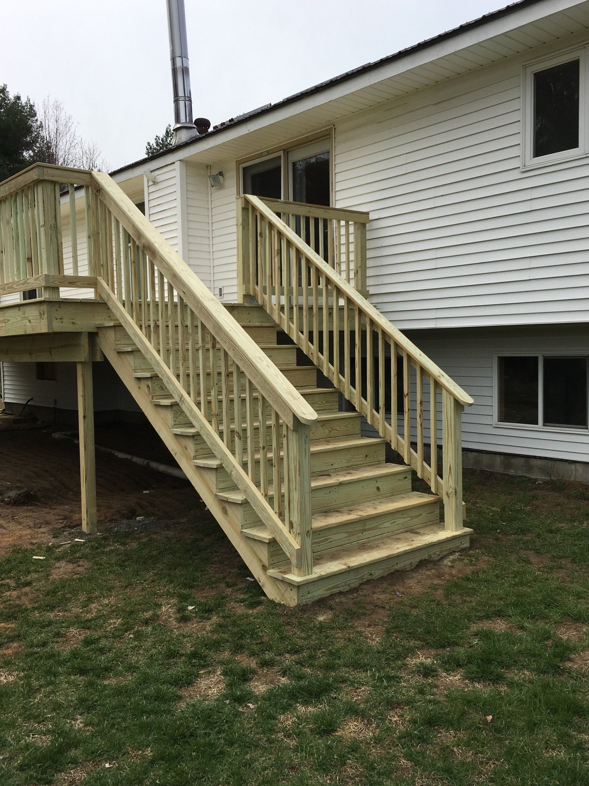 Freshly built wooden accessibility ramp and stairs attached to a white house.