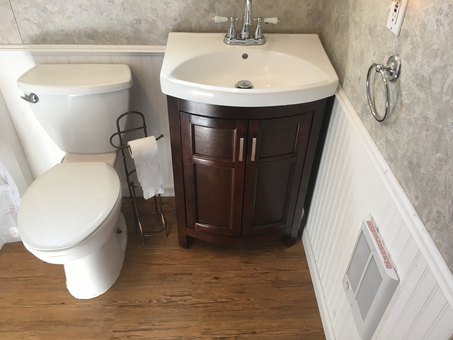 Small bathroom with toilet, sink vanity, and wood-look floor beside a wall vent.