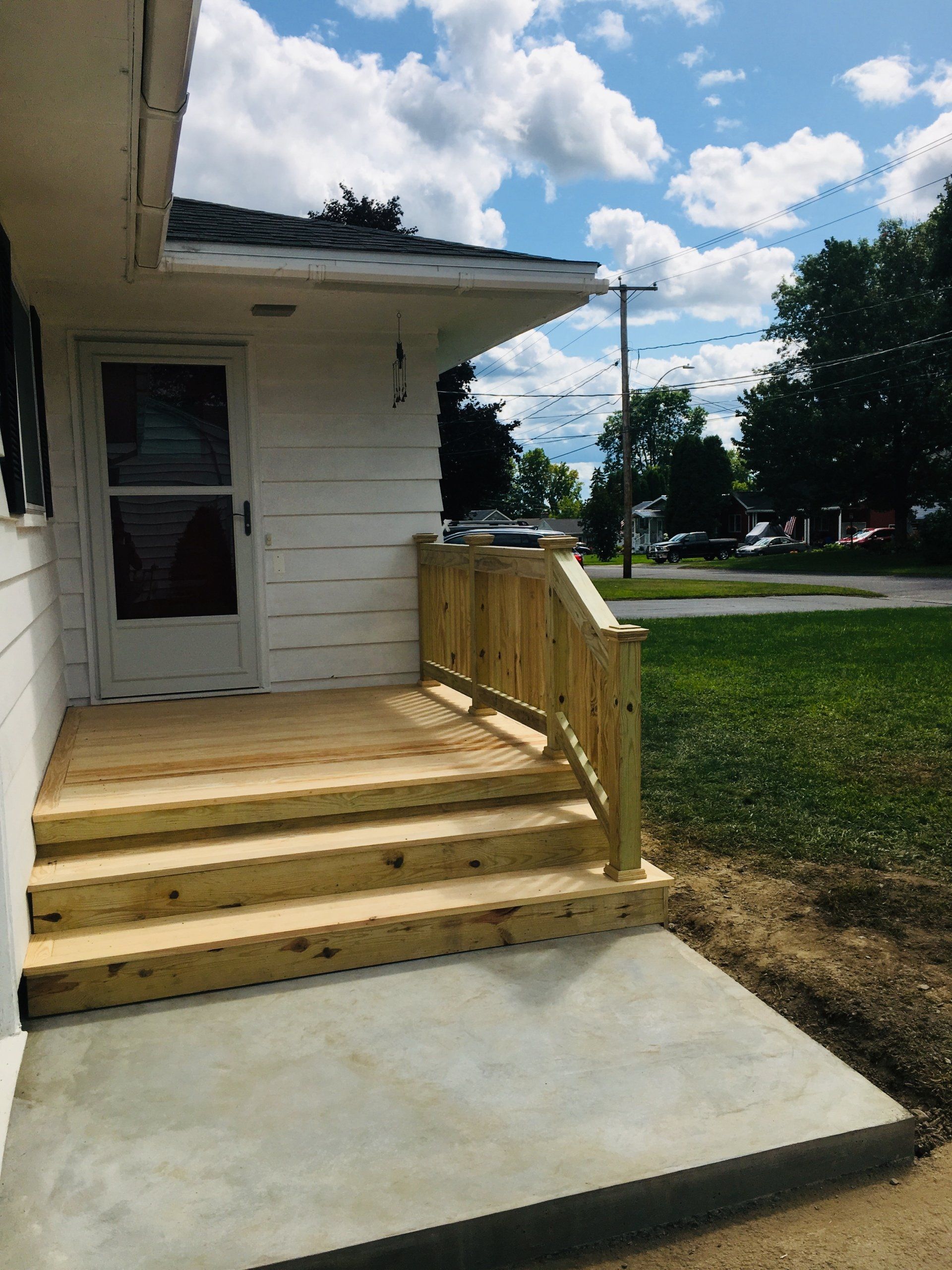 Front porch with wooden steps and railing on a white house beside a concrete walkway and grassy yard