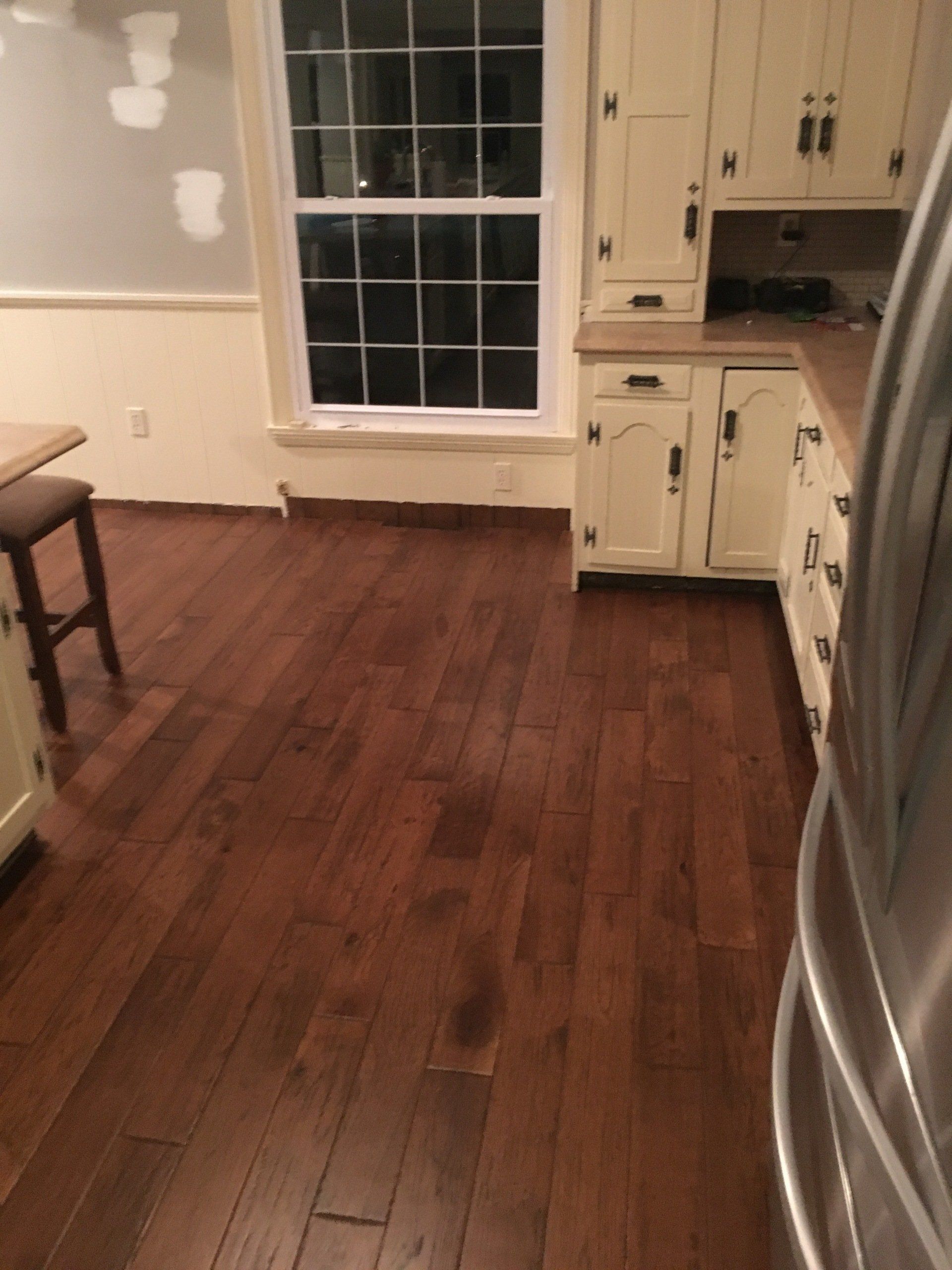 Empty kitchen with dark hardwood floors, white cabinets, and a large window.
