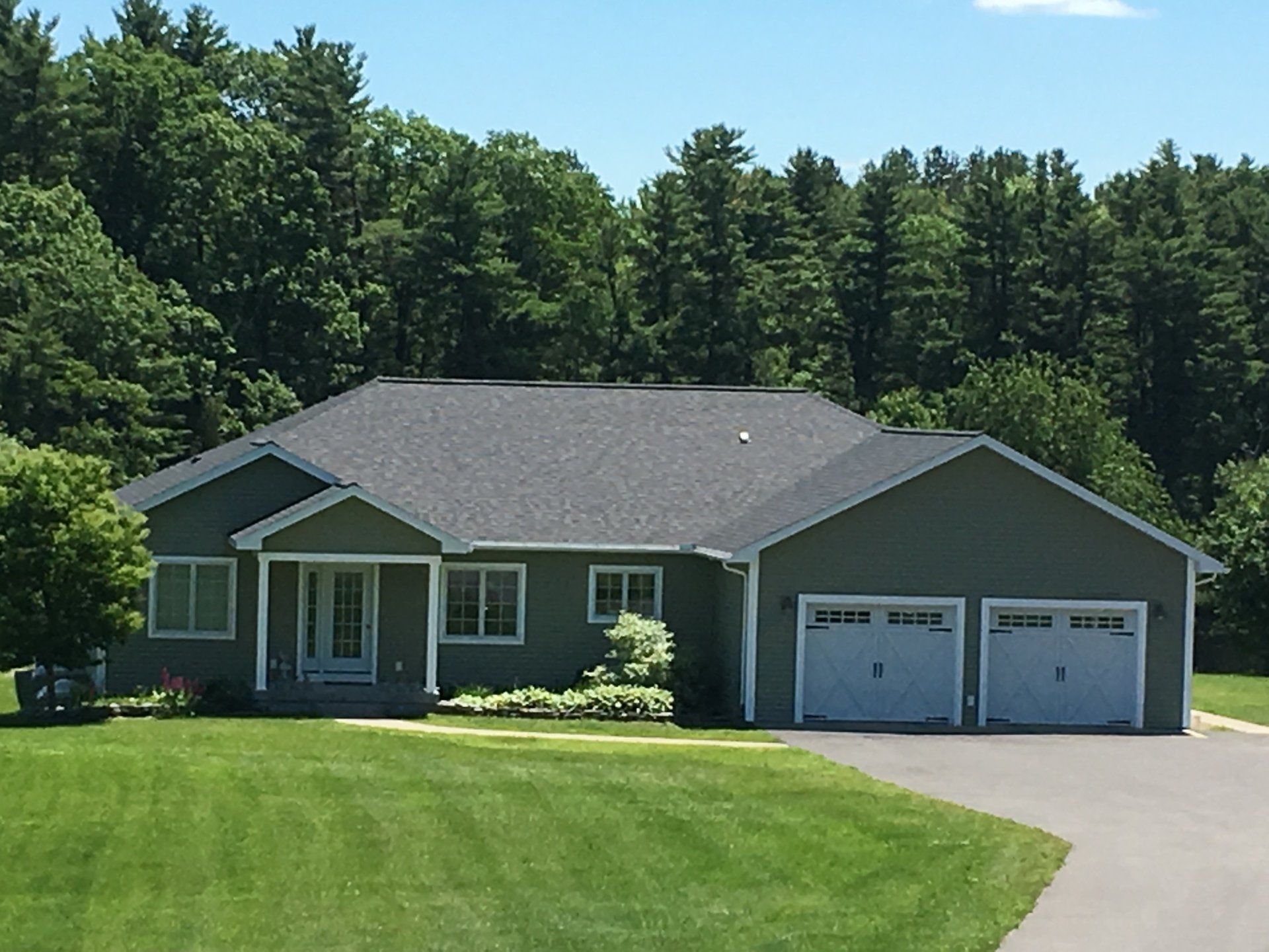 Single-story gray house with two-car garage and a large green lawn under a blue sky
