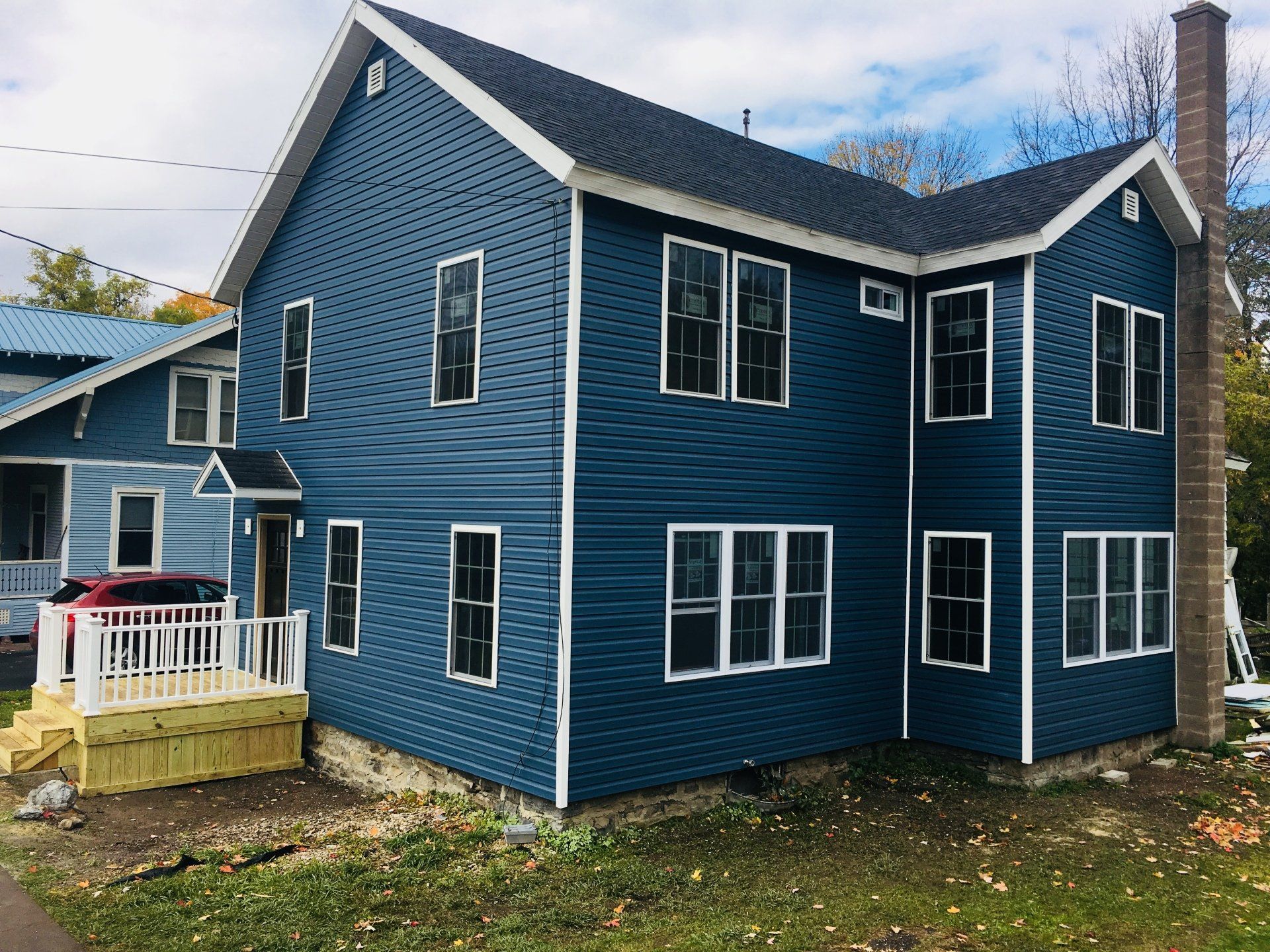 Blue two-story house with white trim, a small porch, and a brick chimney in a yard with bare trees.