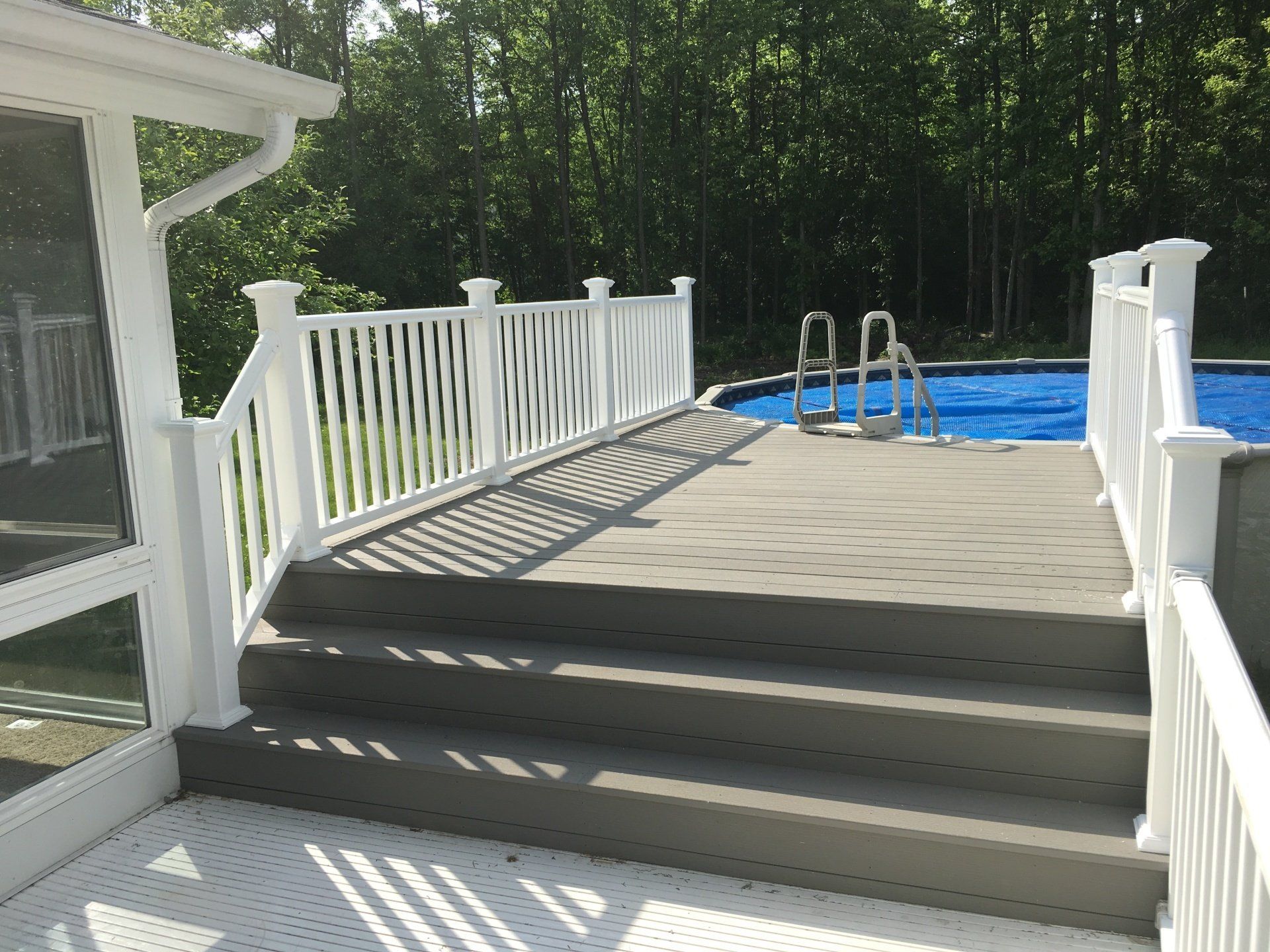 Back deck with white railing, steps, and a blue swimming pool surrounded by trees