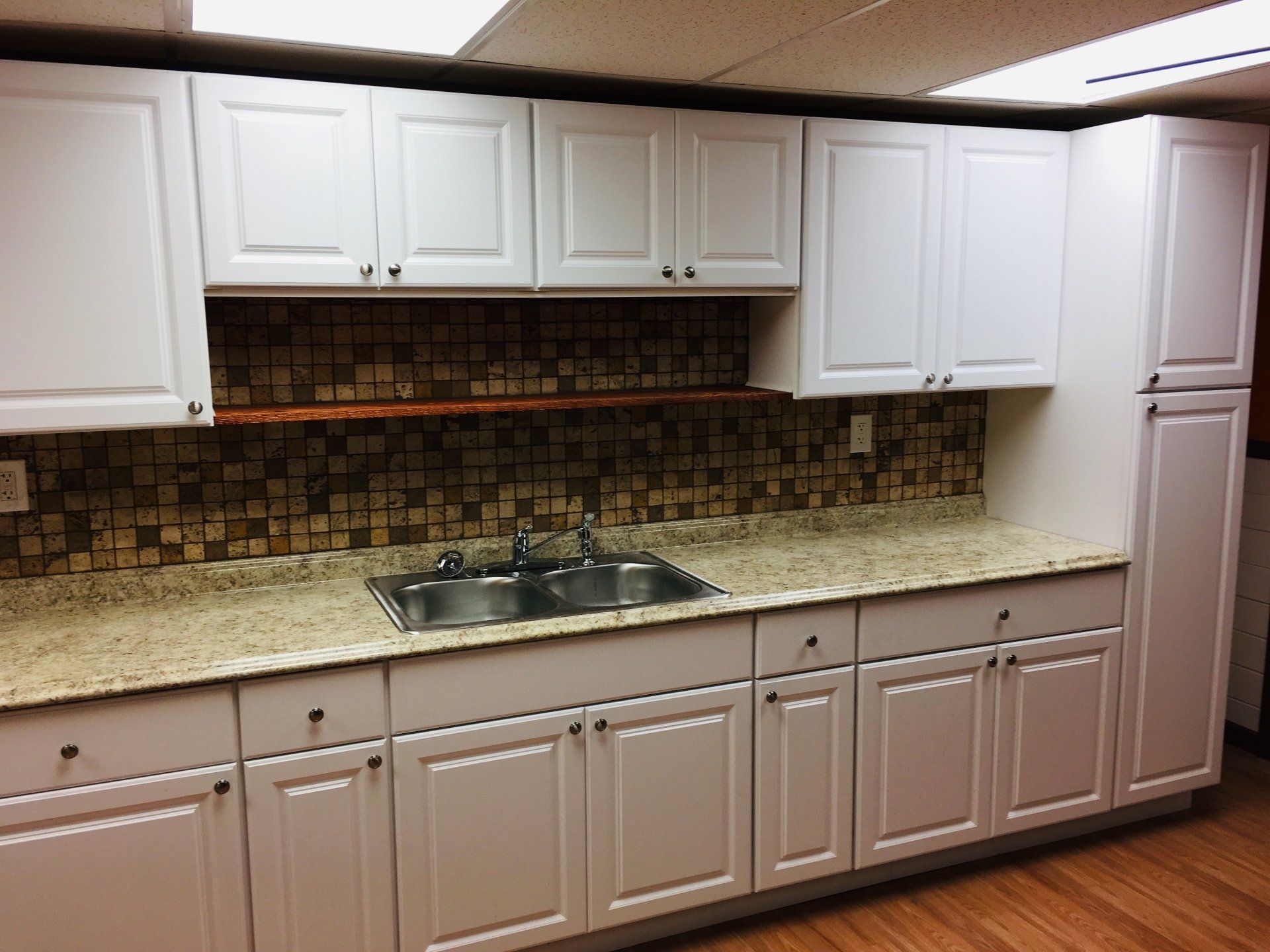 Kitchen with white cabinets, beige countertop, mosaic backsplash, and double sink under a pass-through opening