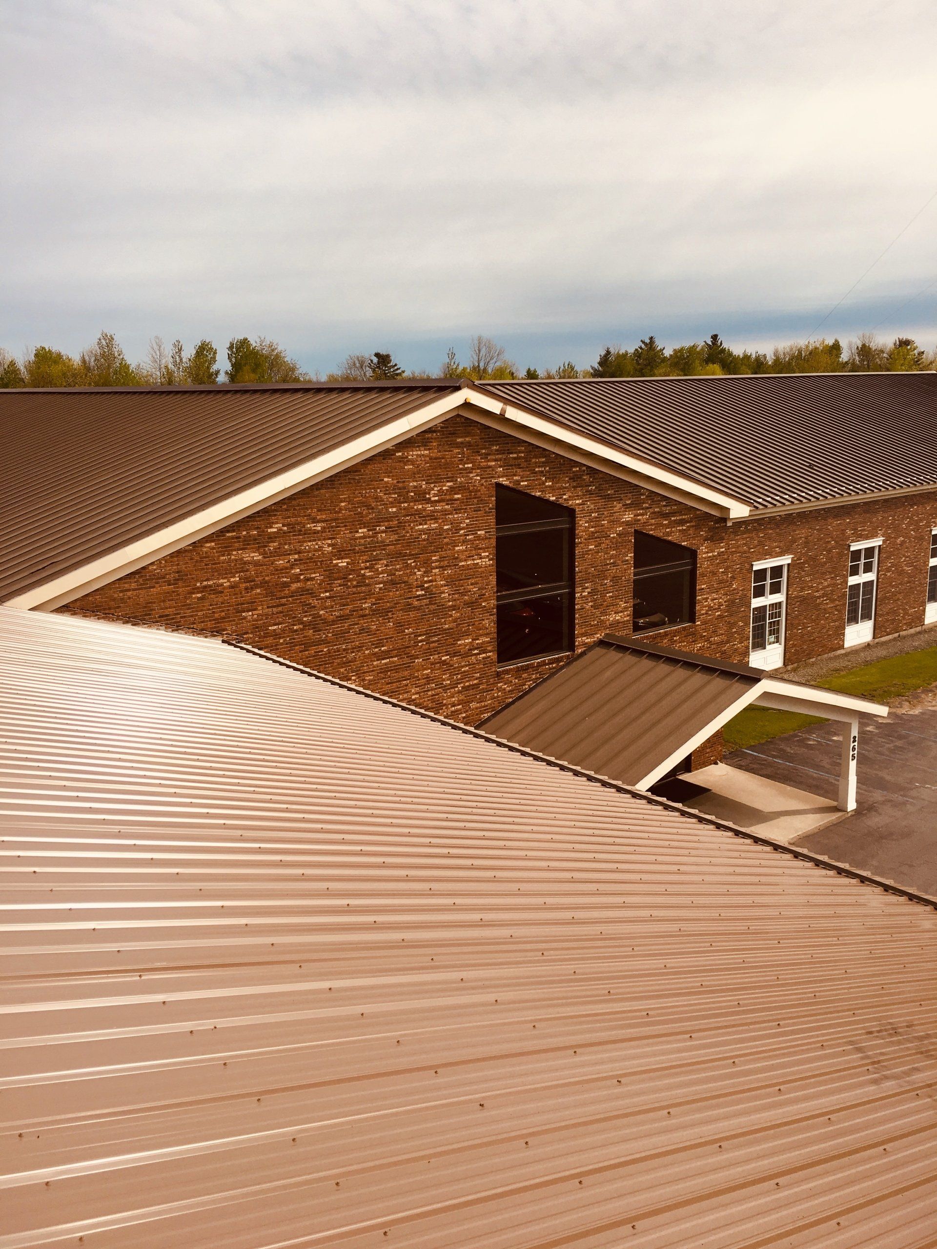 A red brick building with a tan corrugated roof and a small covered entrance under a cloudy sky.