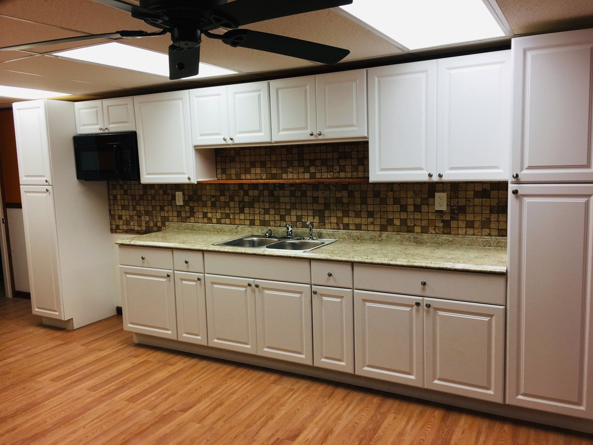 Empty kitchen with white cabinets, beige tile backsplash, and wood flooring