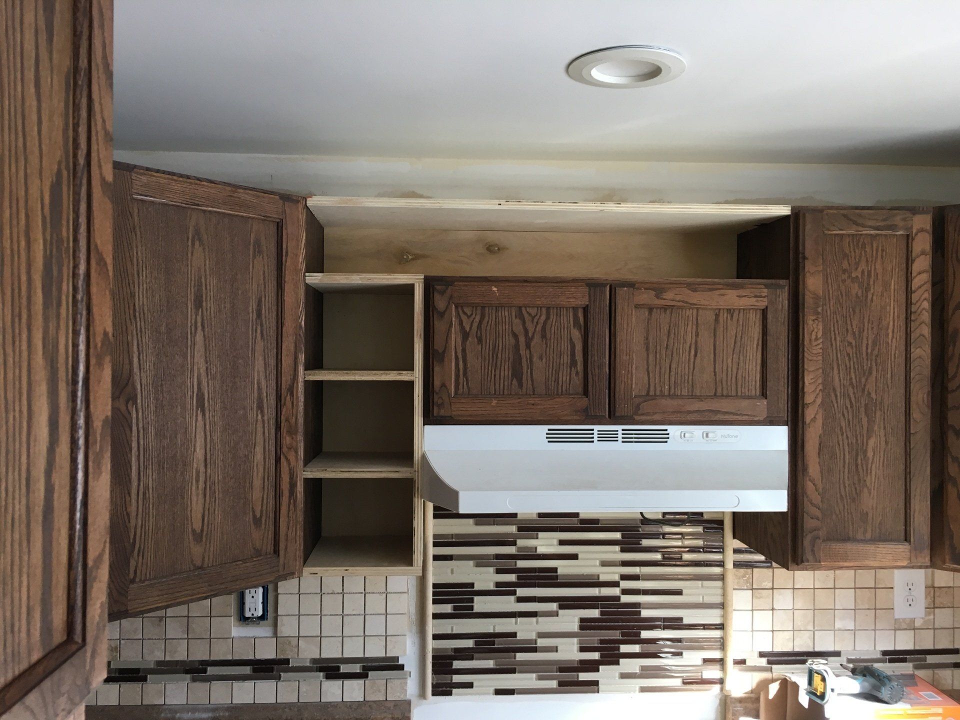 Small kitchen with dark wood cabinets, white range hood, tiled backsplash, and recessed ceiling light.
