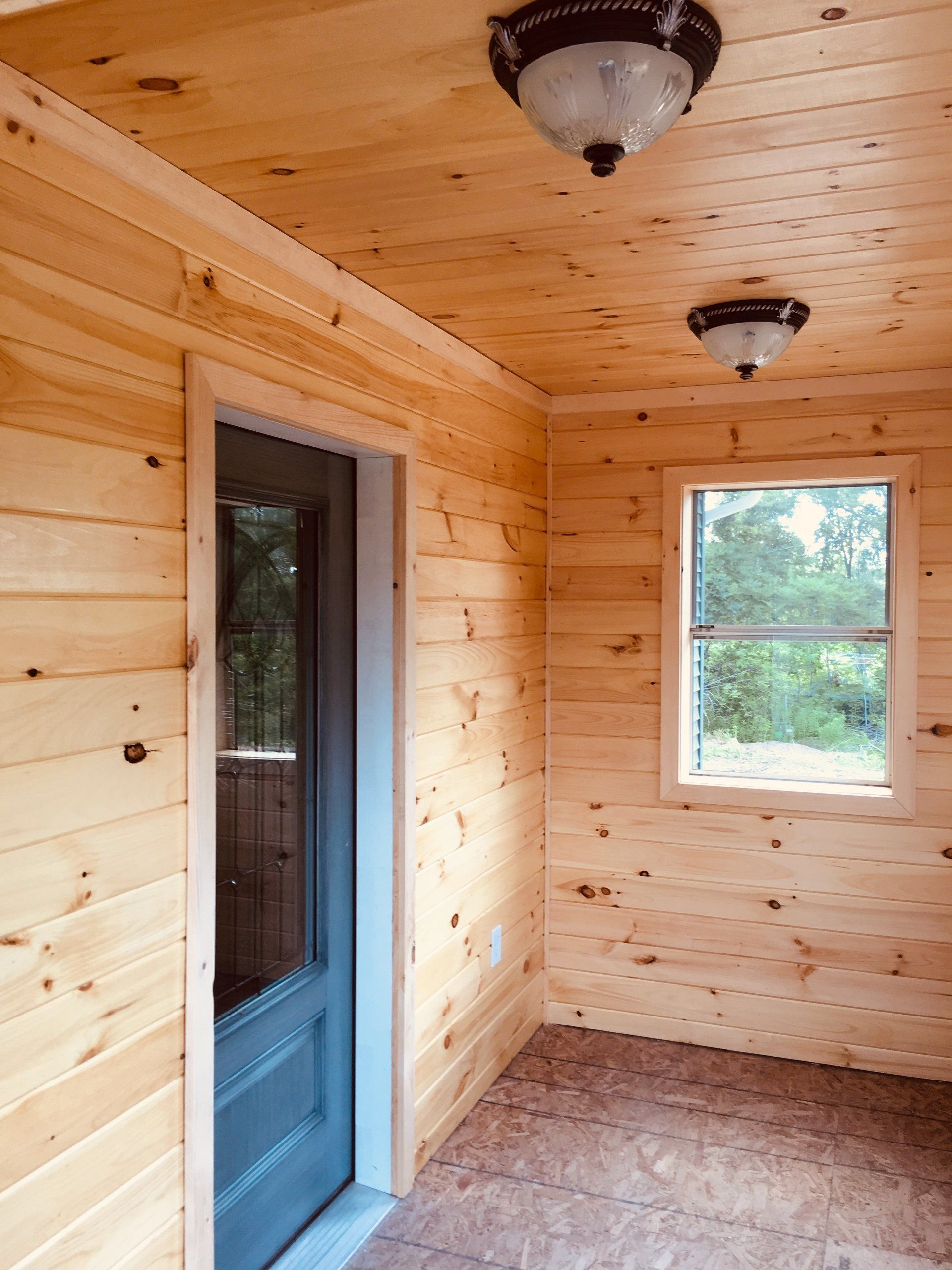 Small wood-paneled room with a glass door, window, and two ceiling light fixtures.