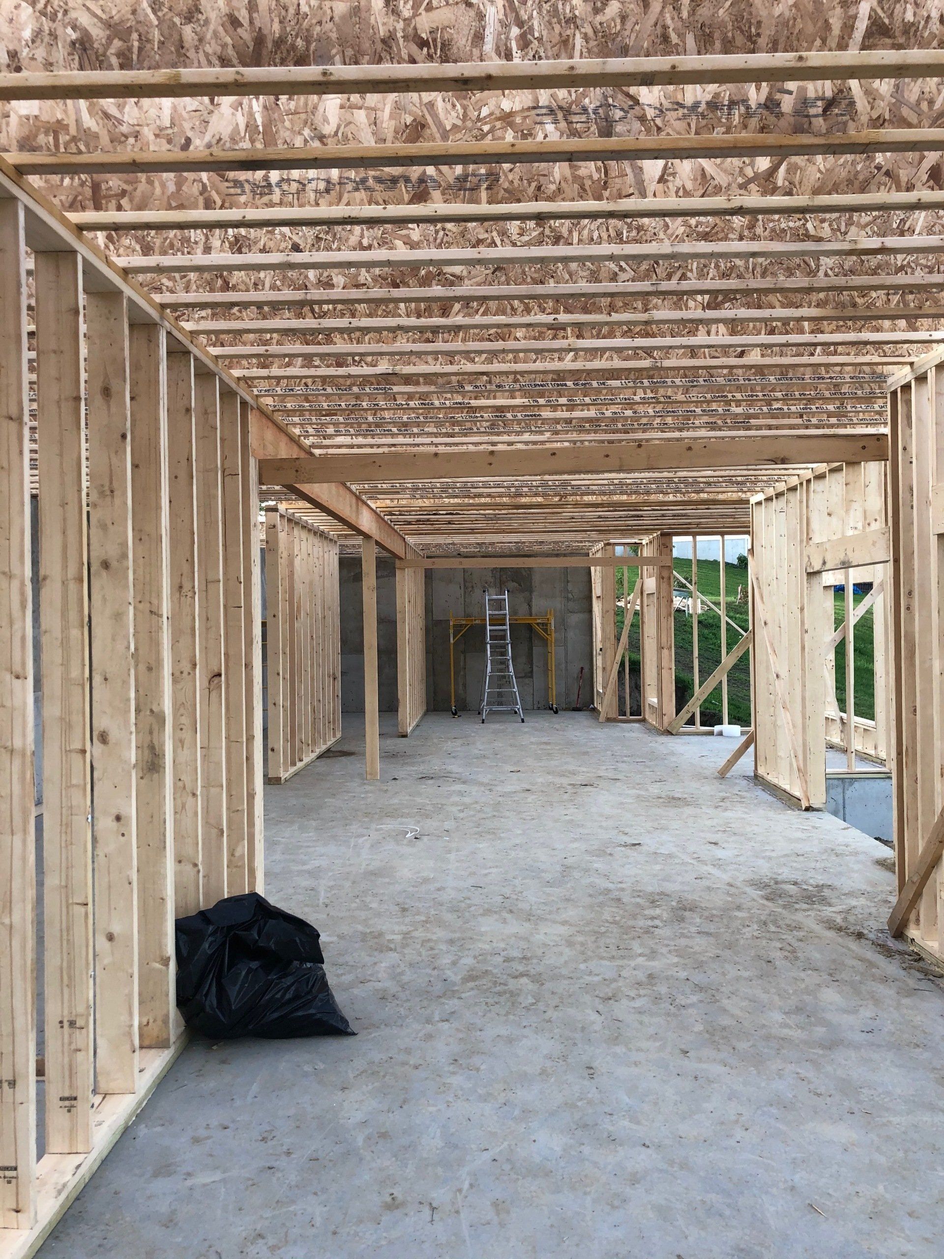 Interior of a wood-framed building under construction with exposed beams and a concrete floor