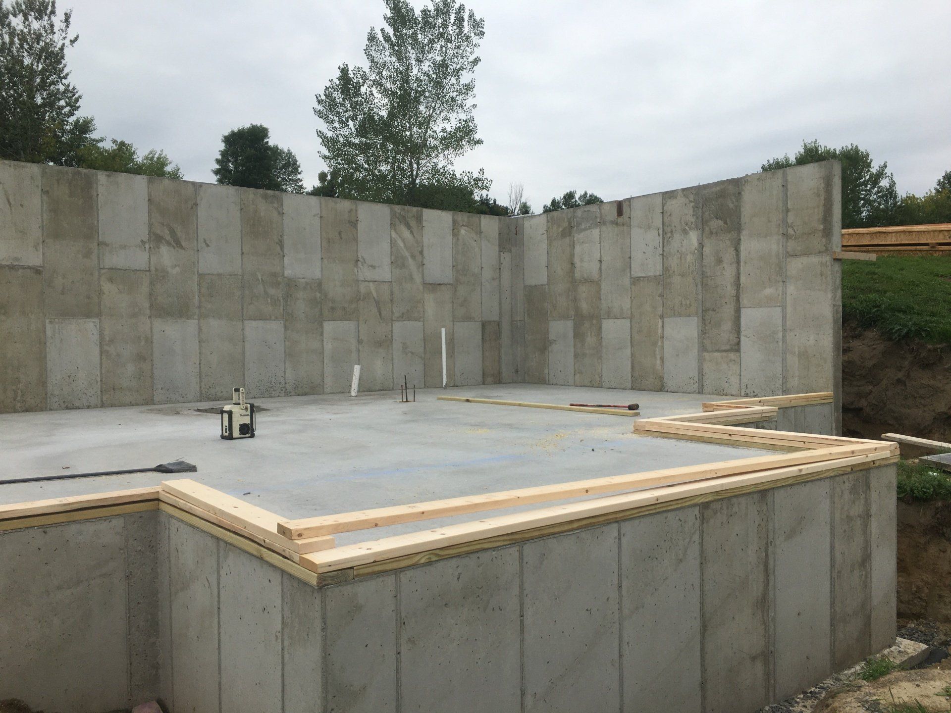 Concrete foundation slab at a construction site with tall retaining walls and trees in the background