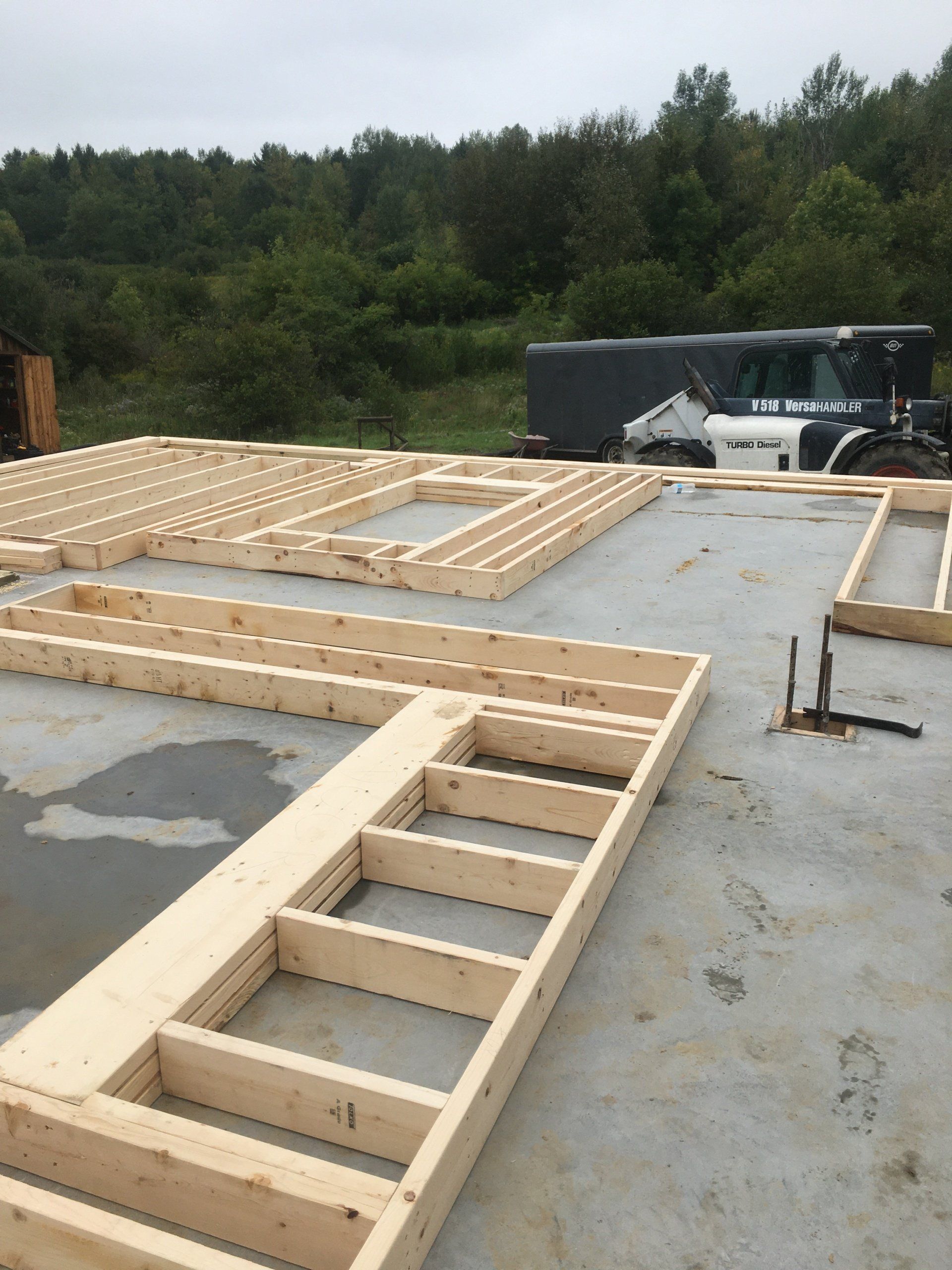 Wood framing for house walls laid out on a concrete slab at a construction site.