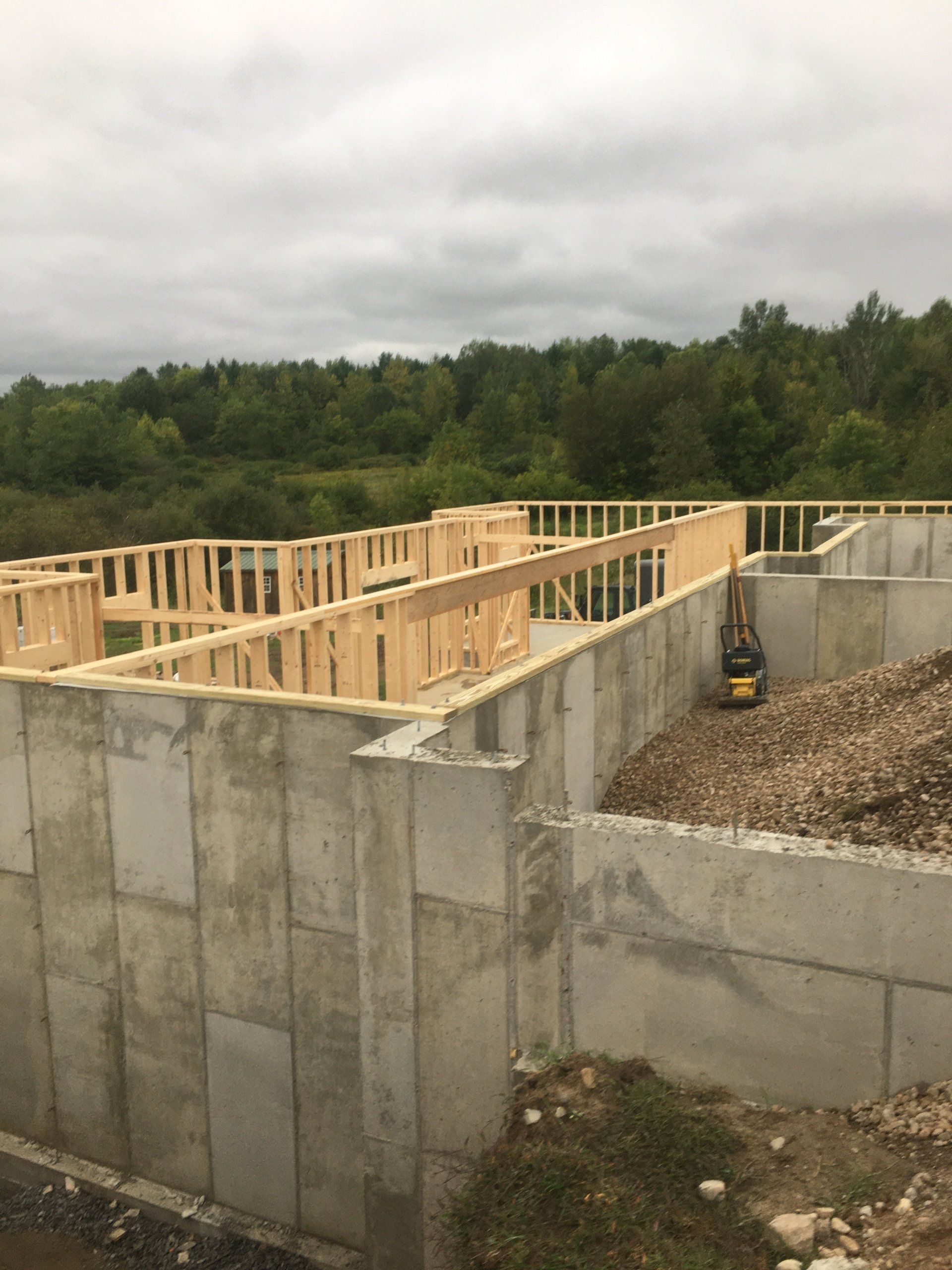 Concrete foundation with wooden framing under construction, surrounded by trees and cloudy sky.