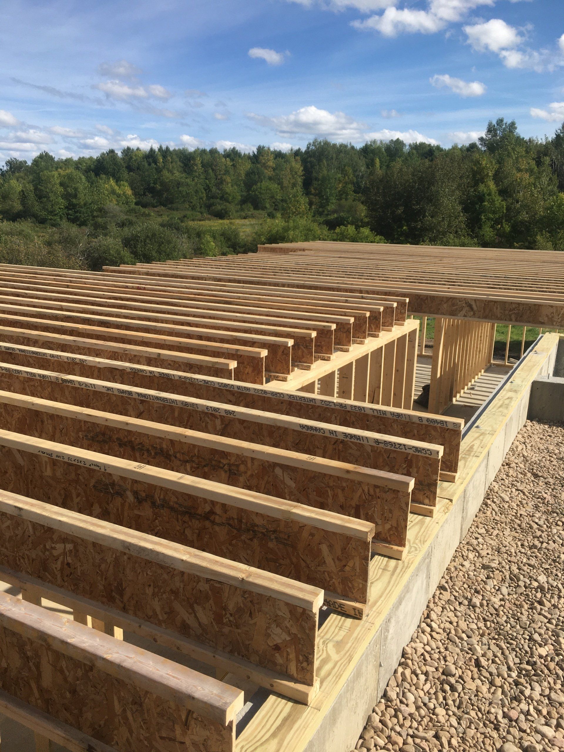 Wooden roof framing under construction on a building site with trees and blue sky in the background