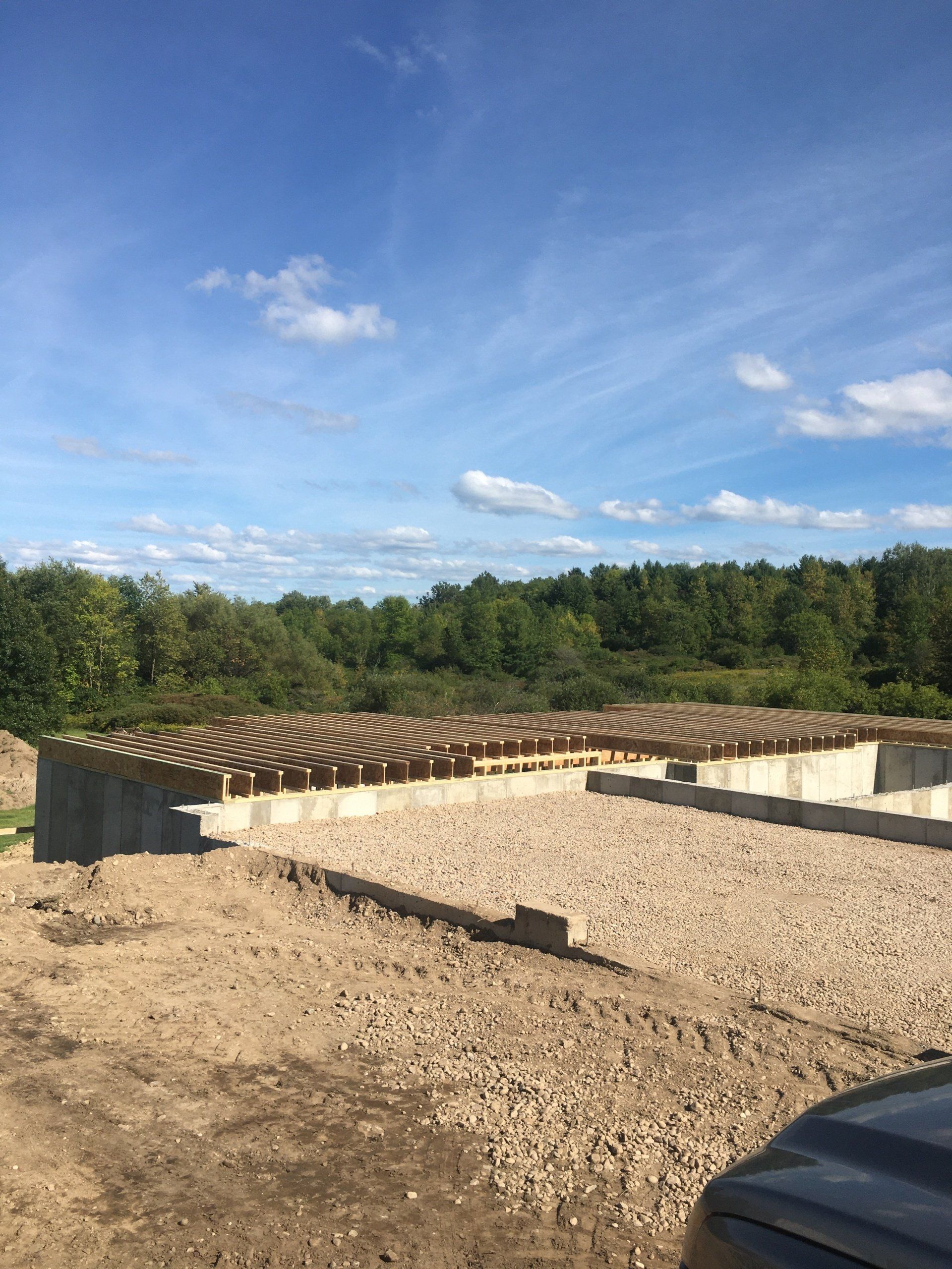 Construction site with a foundation trench, dirt piles, and a blue sky over trees