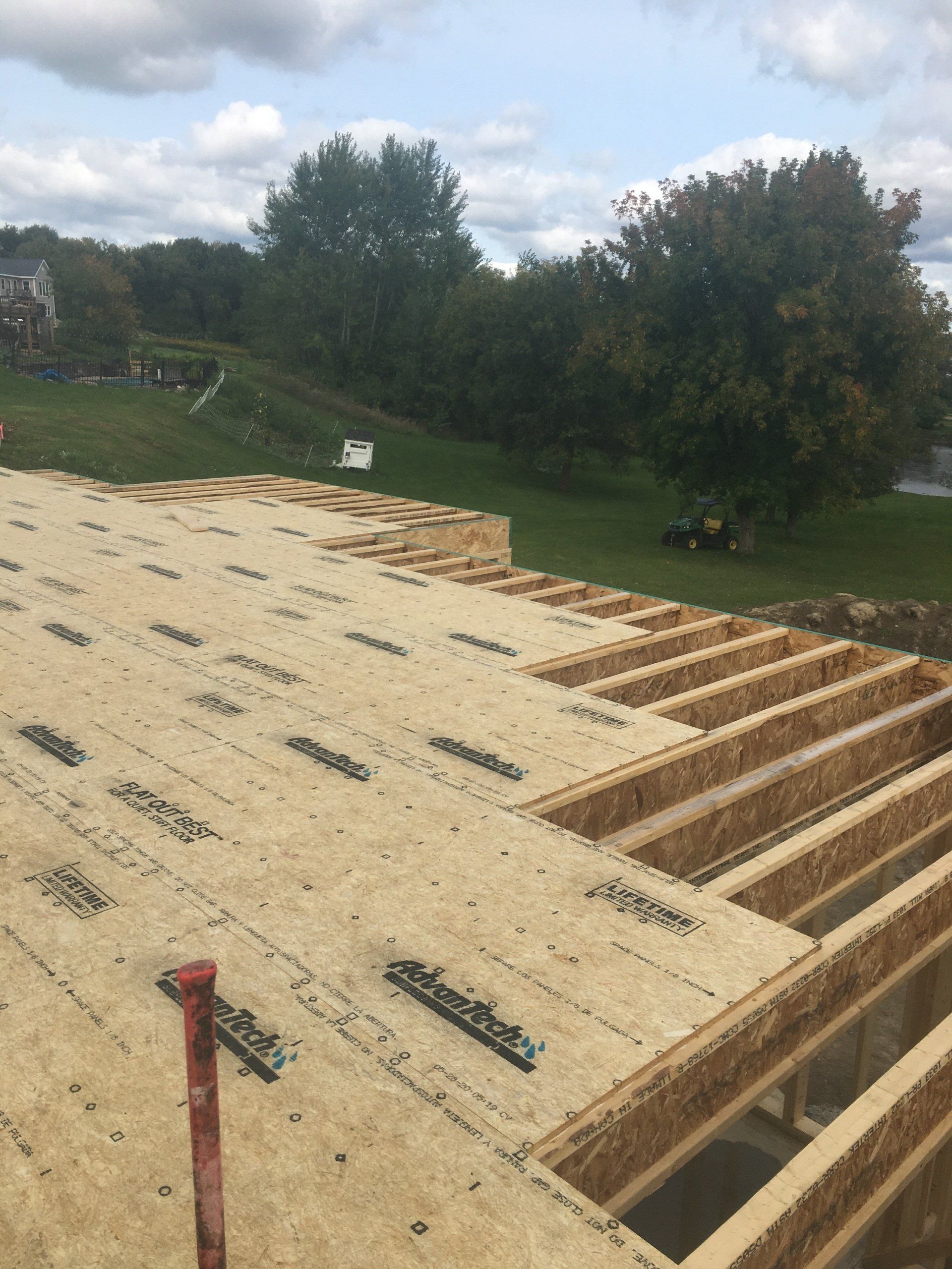 Roof under construction with plywood sheathing and exposed framing beside a grassy yard
