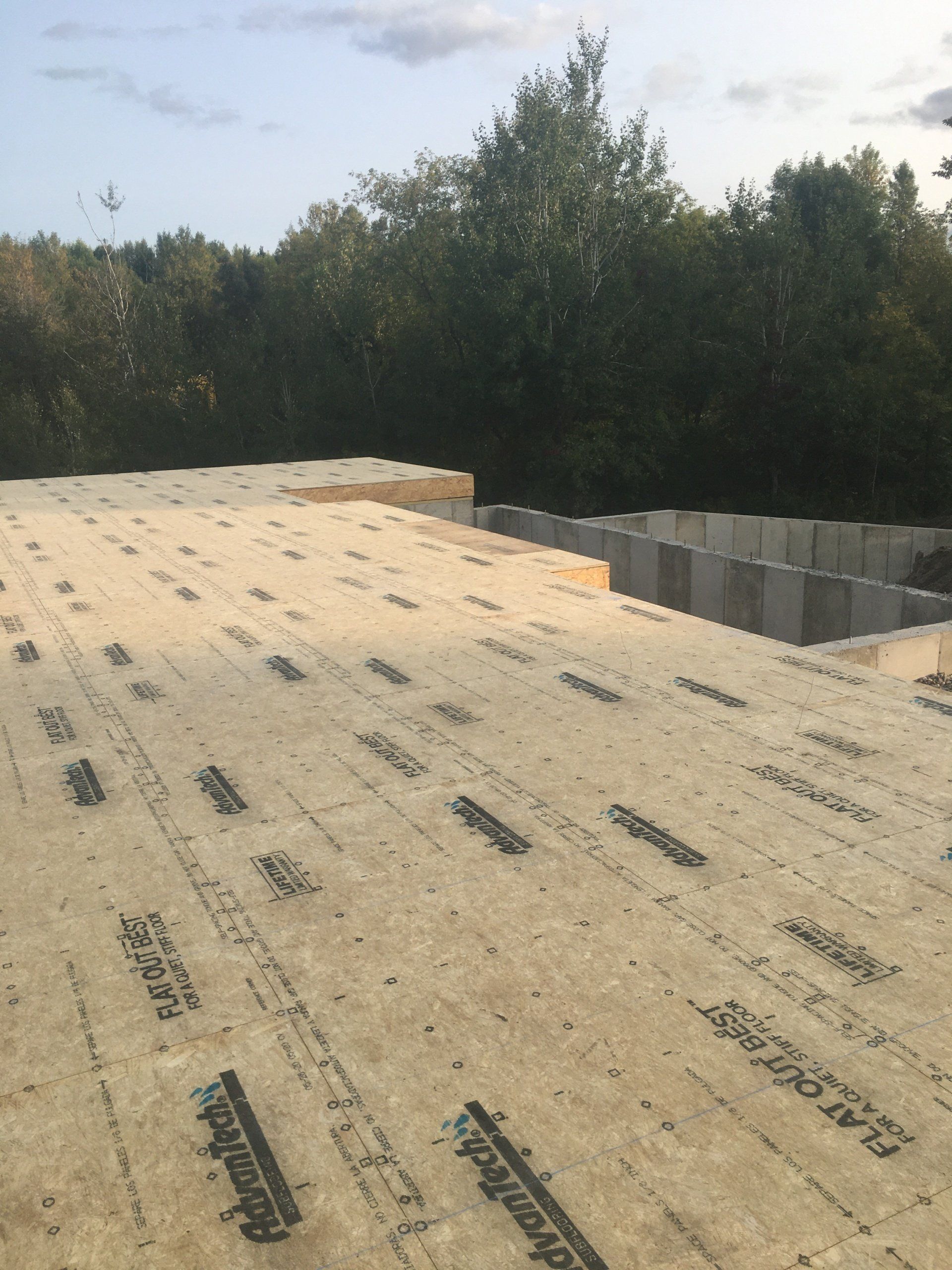 Partially installed roofing underlayment on a sloped roof with trees in the background