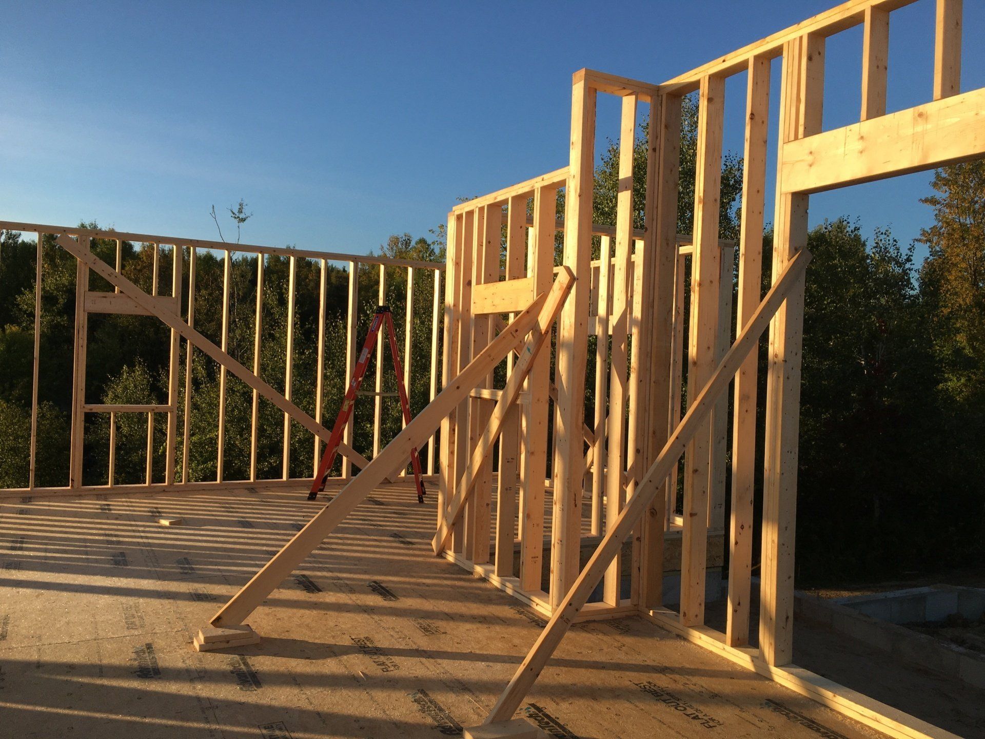Wood-framed house under construction in sunlight, with unfinished walls and roof framing.