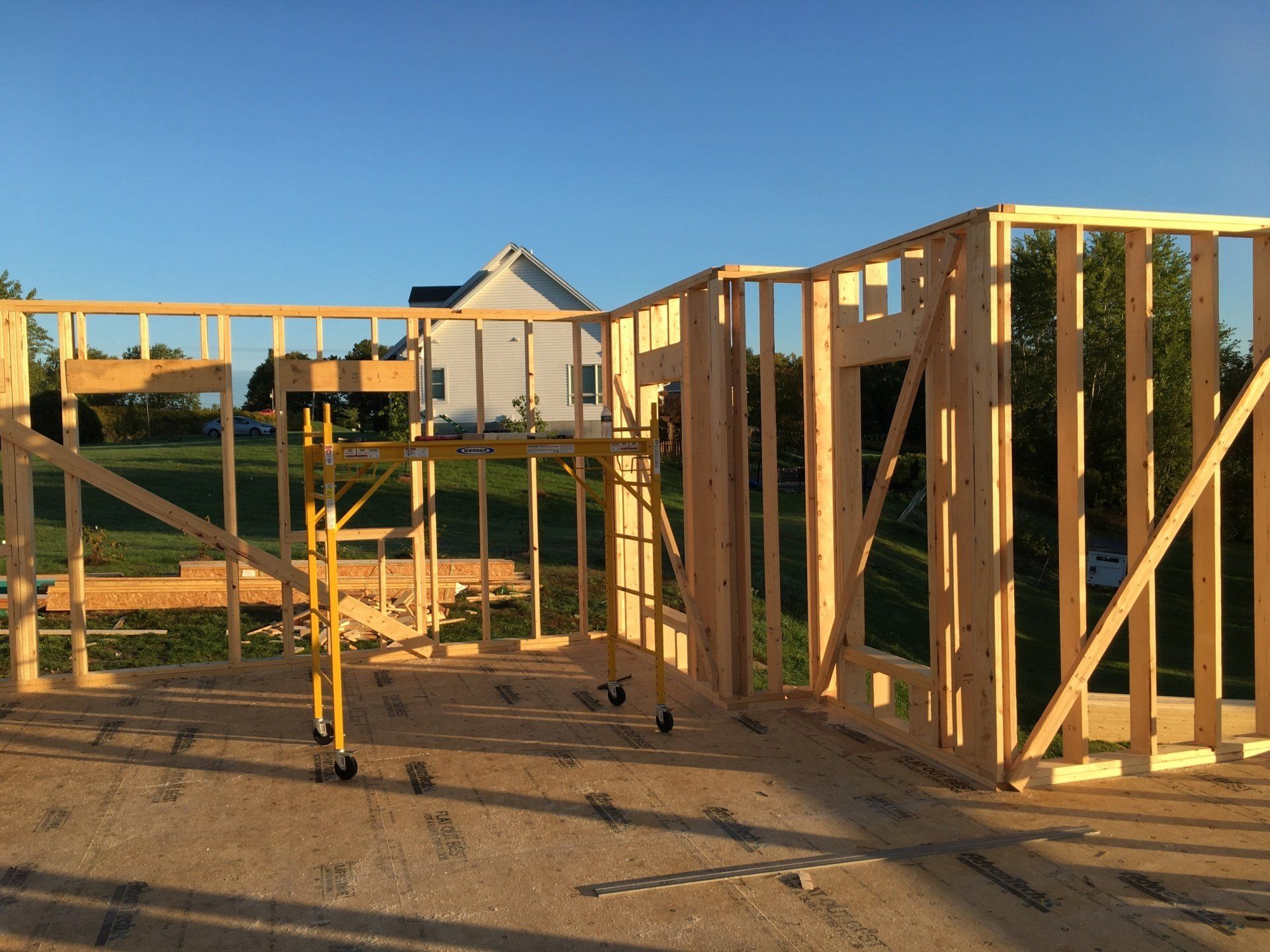 Wooden house framing under construction at sunset, with scaffolding on a concrete foundation.