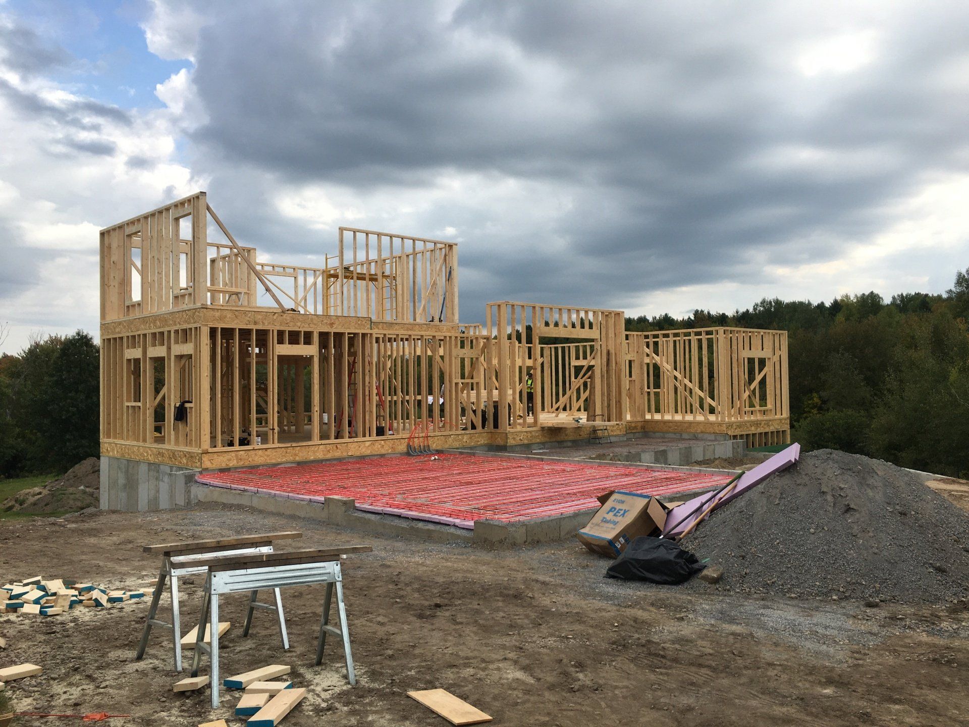 House under construction with wooden framing, red foundation wrap, and gravel site under cloudy sky