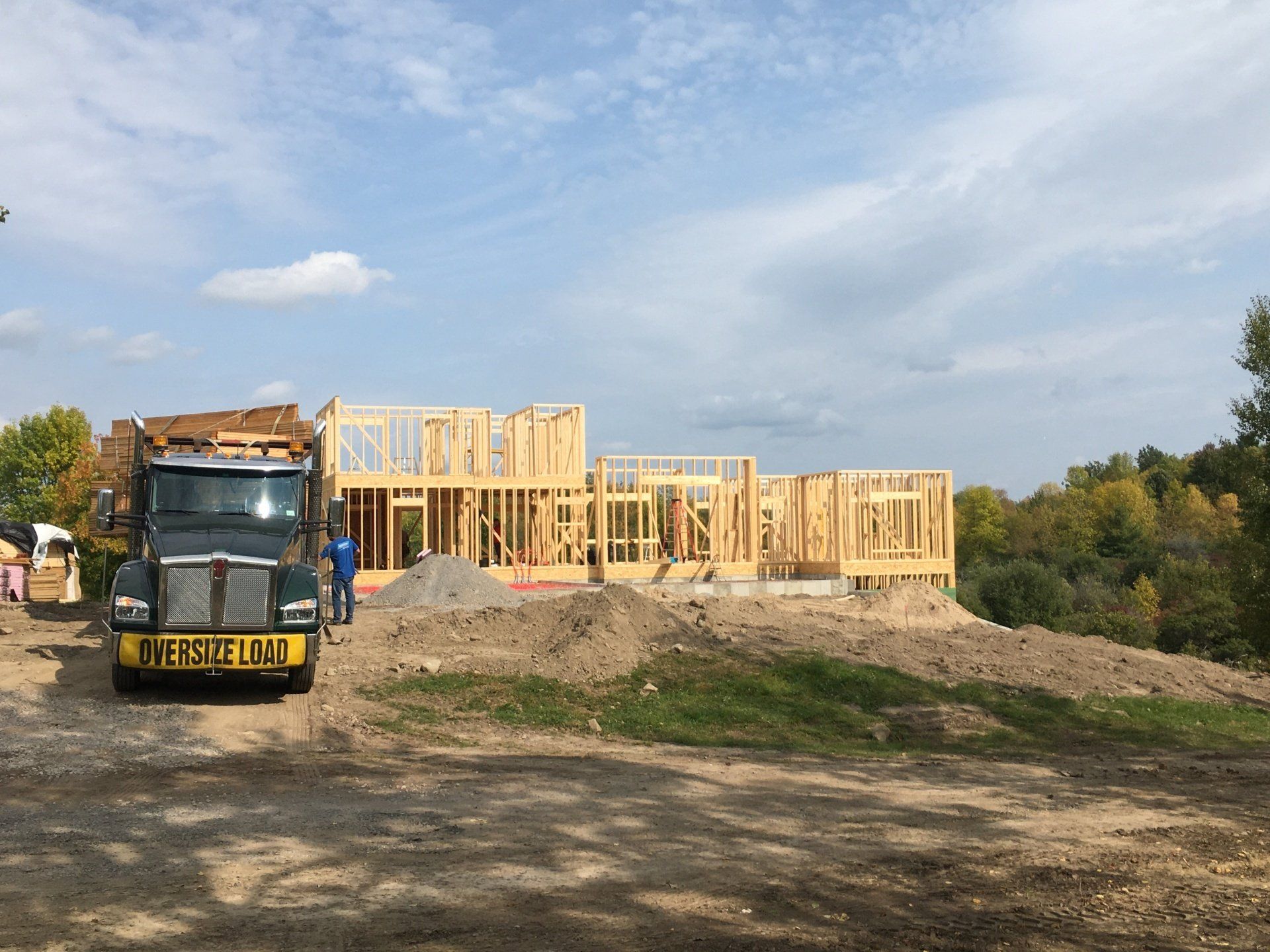 Construction site with wooden house framing, dump truck, and workers under a blue sky