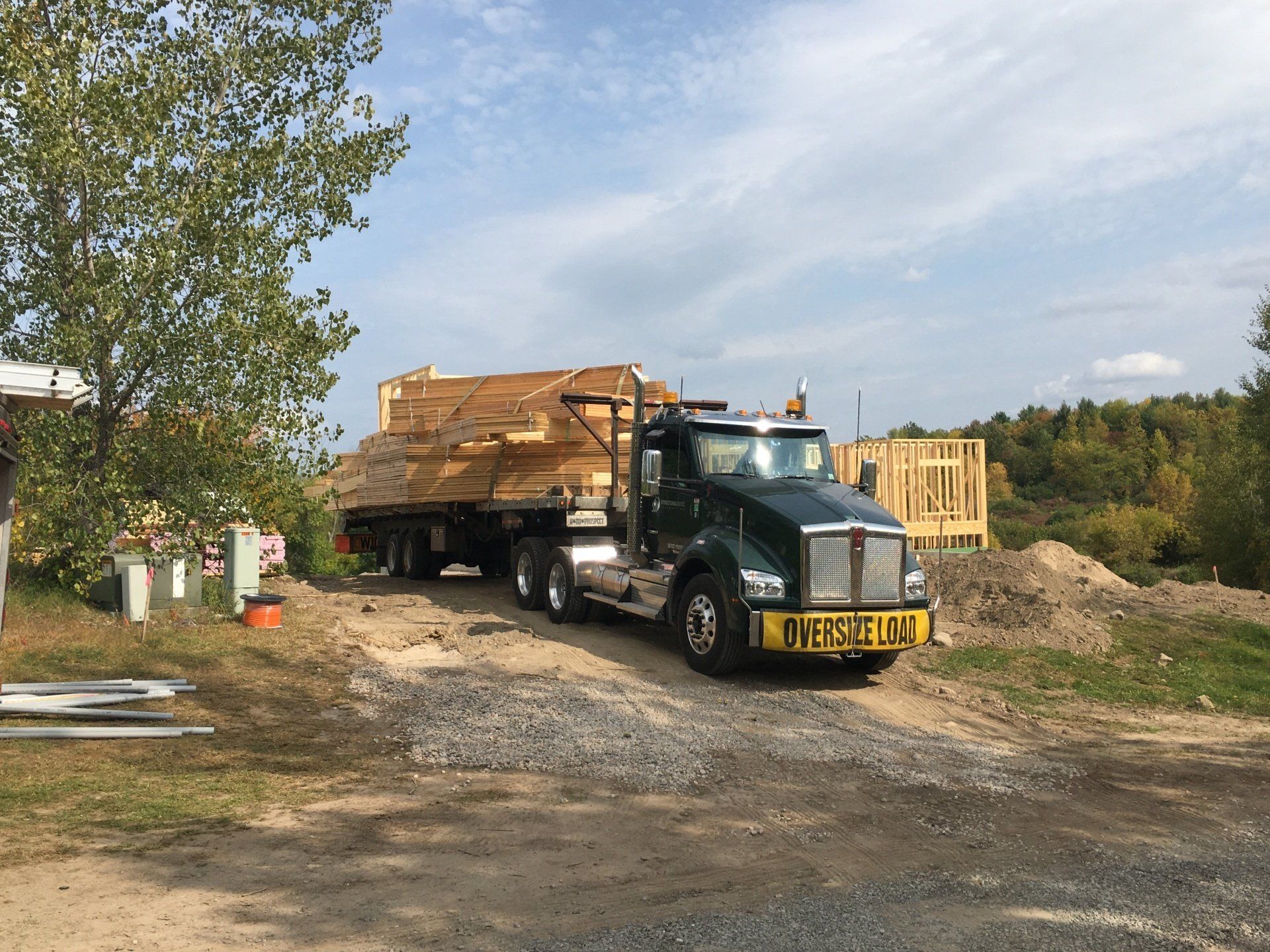 Black dump truck loaded with wood scraps parked on a dirt lot under a partly cloudy sky