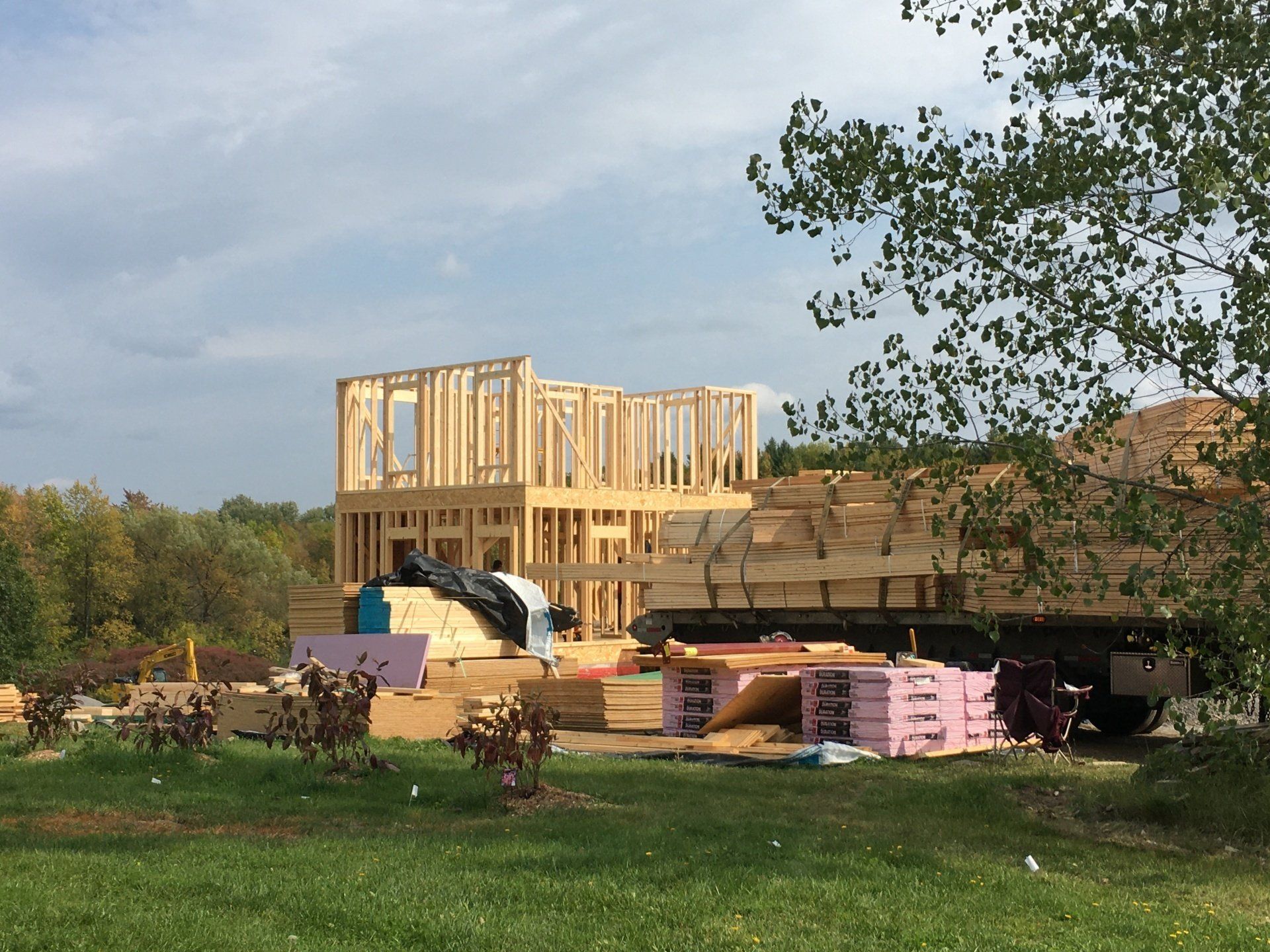 Partially built wooden house on a construction site with lumber piles and a blue sky