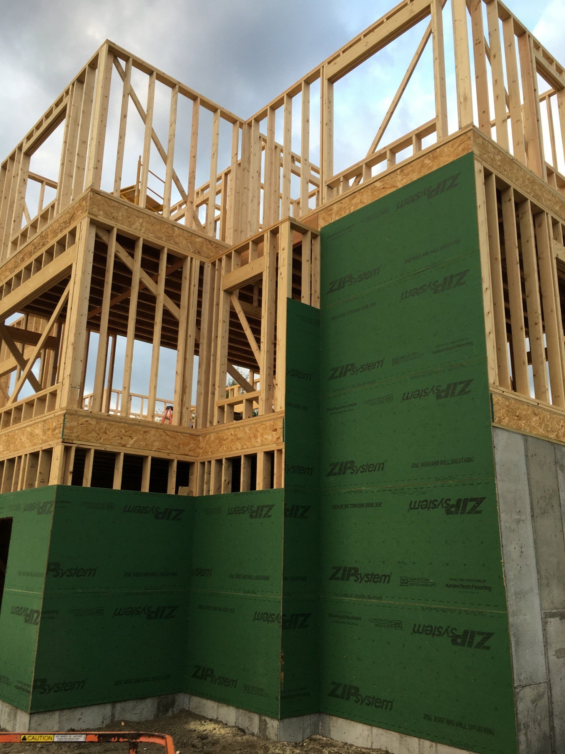 Wood-framed house under construction with green sheathing and exposed upper framing