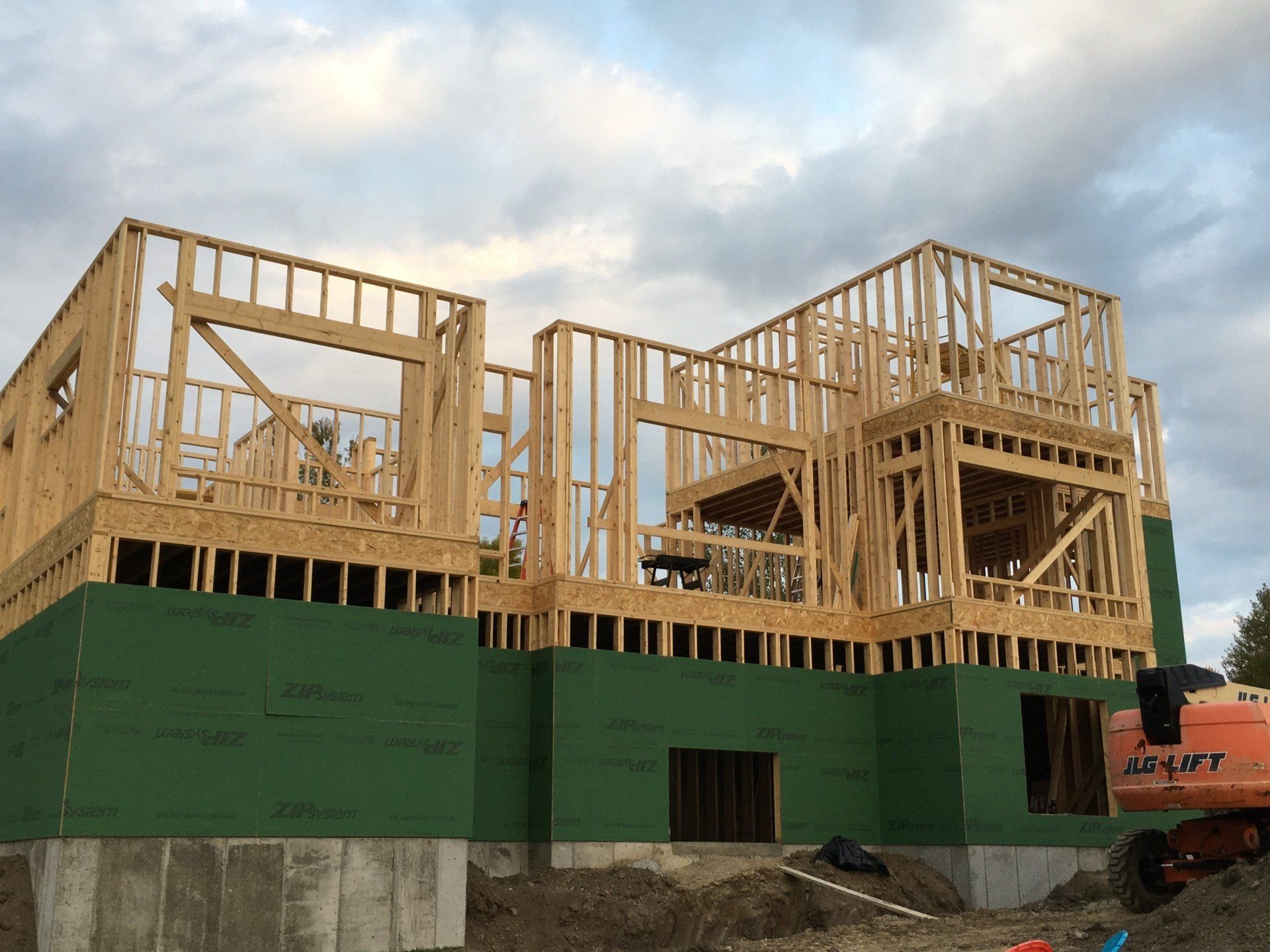 Partially built house with wooden framing and green sheathing under a cloudy sky