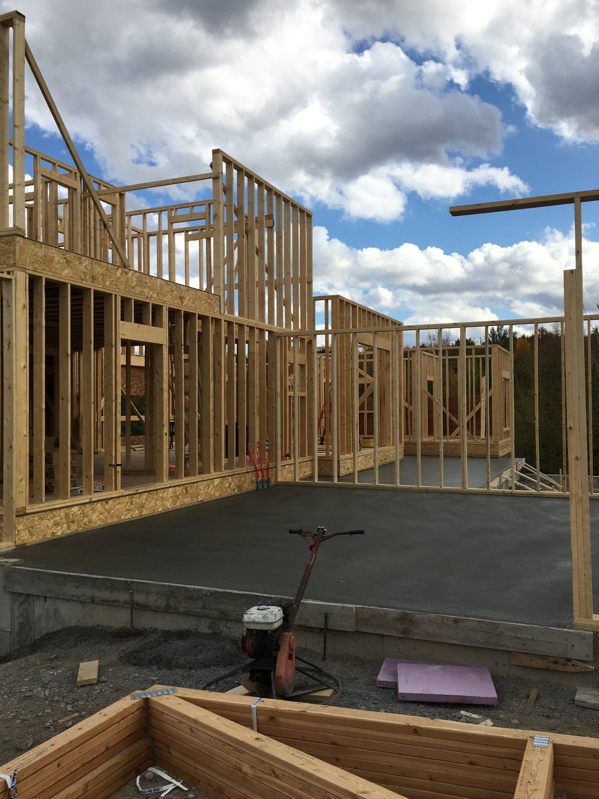 Framed house under construction with wooden studs and a concrete slab under a cloudy sky