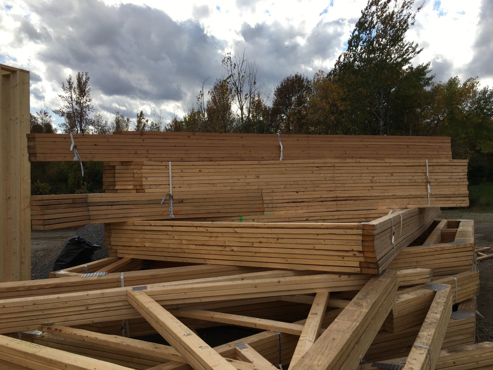 Stacks of lumber and wooden beams at an outdoor construction site under a cloudy sky