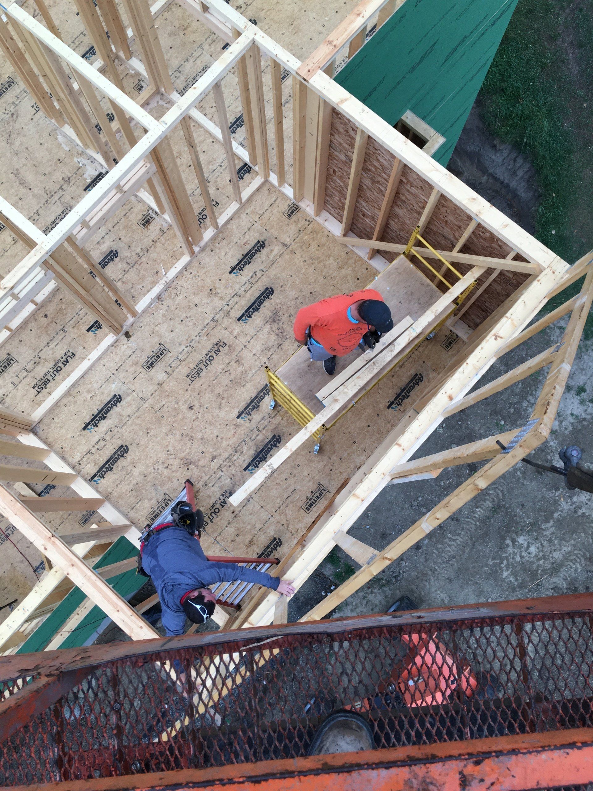 Workers framing a wooden floor of a house under construction, viewed from above.