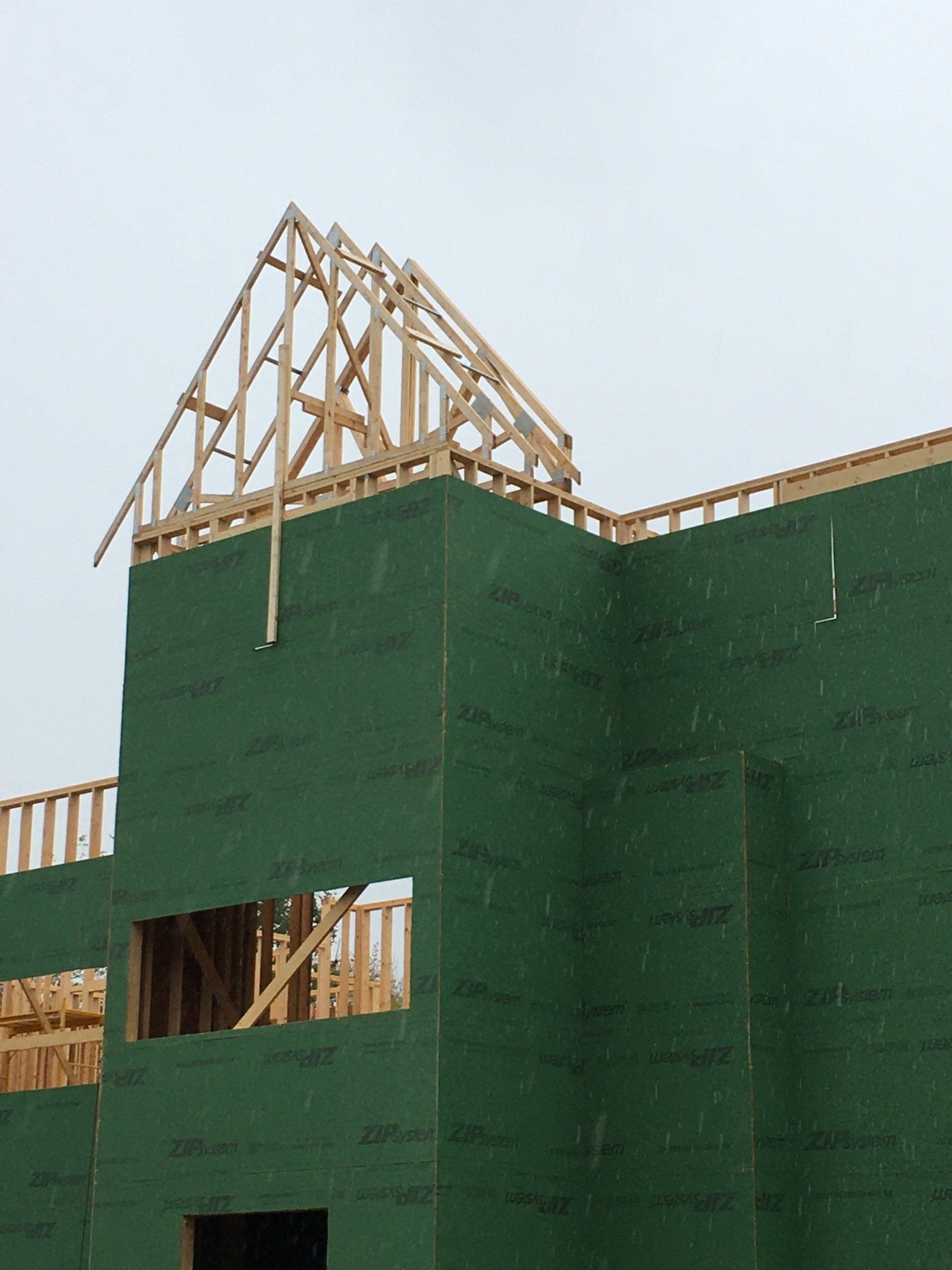 Green construction site with exposed wooden roof framing against a cloudy sky