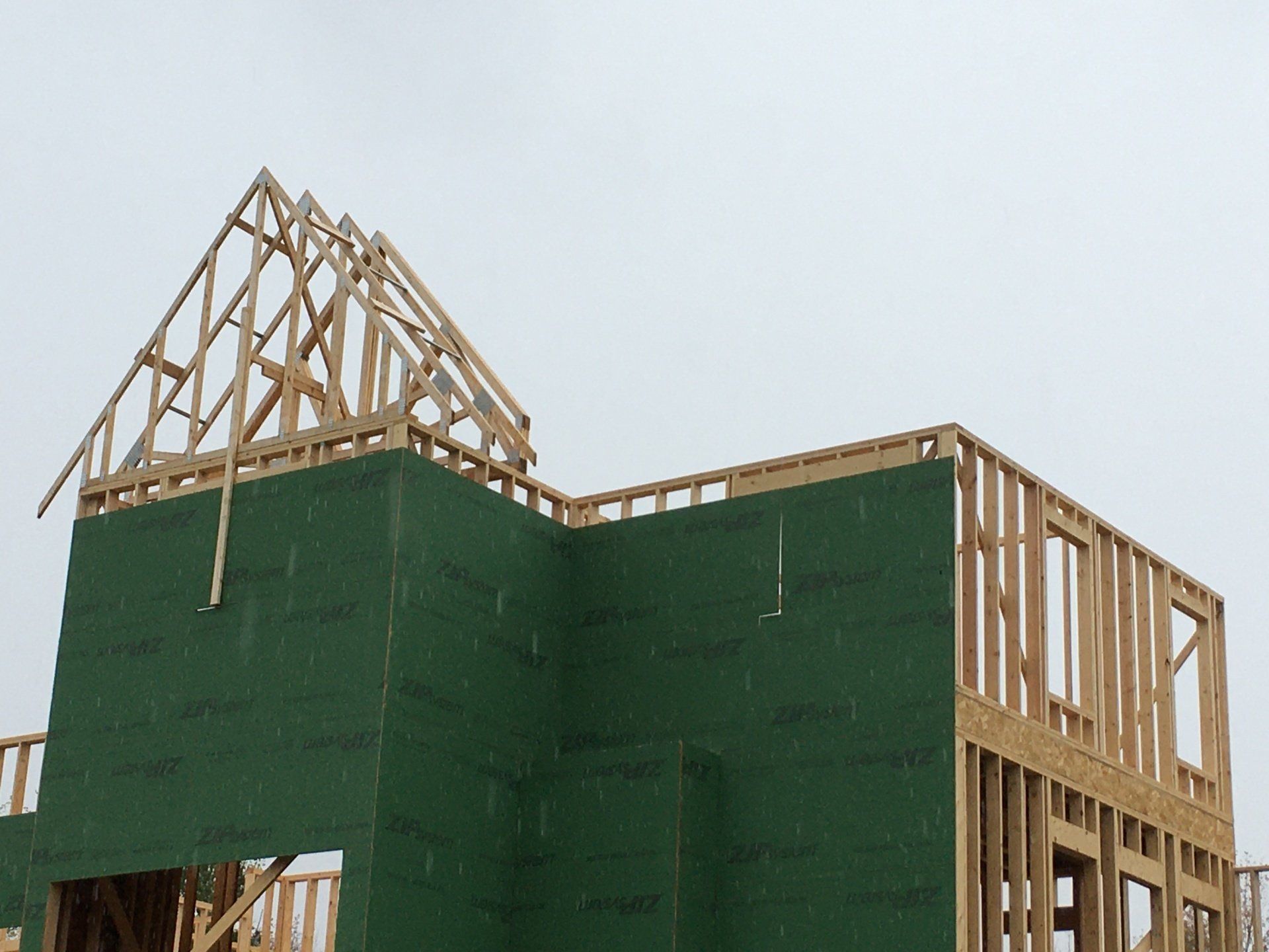 Wood-framed house under construction with green sheathing and exposed roof trusses