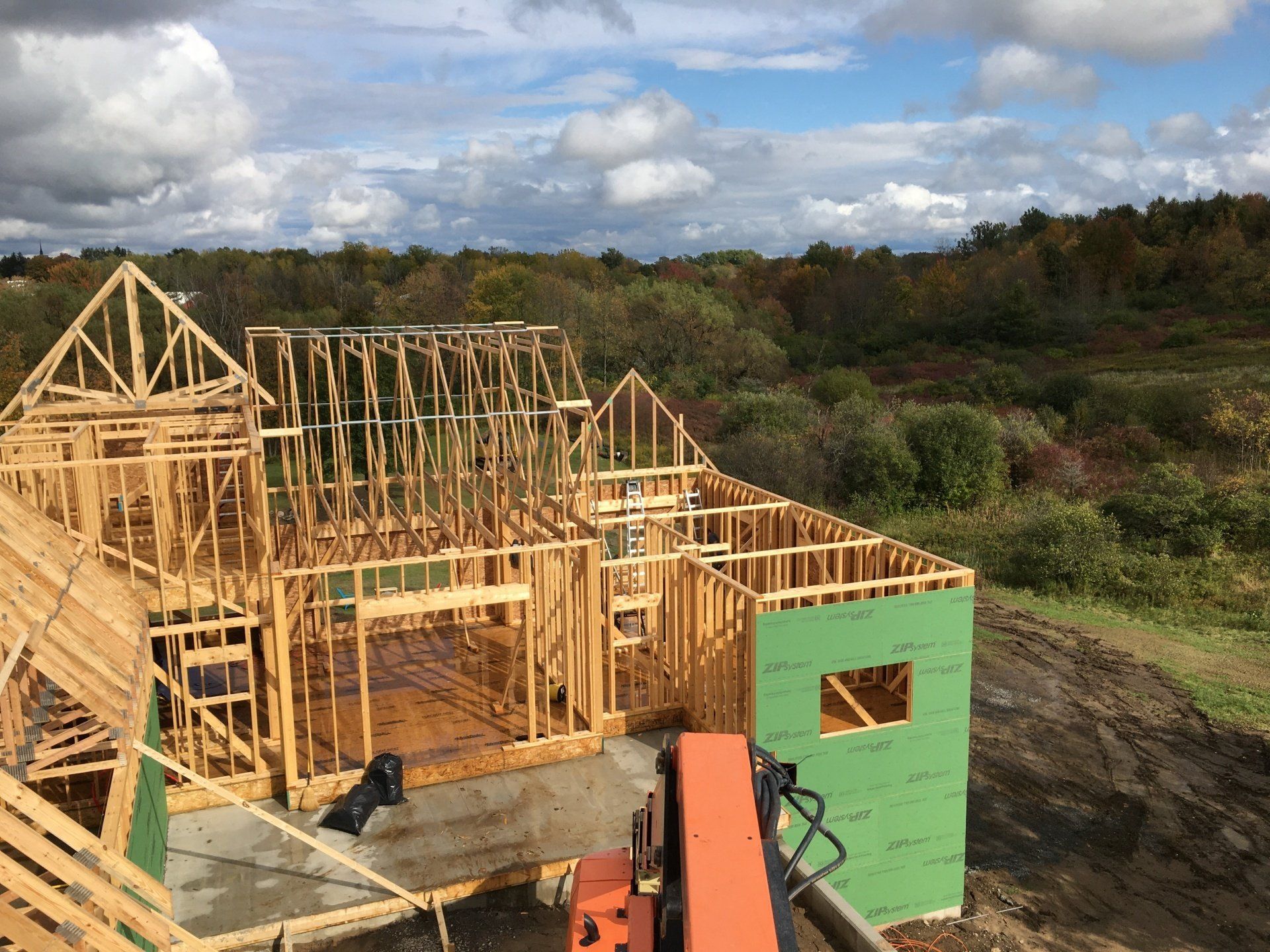 Wood-framed house under construction with green sheathing and an orange ladder in a rural field